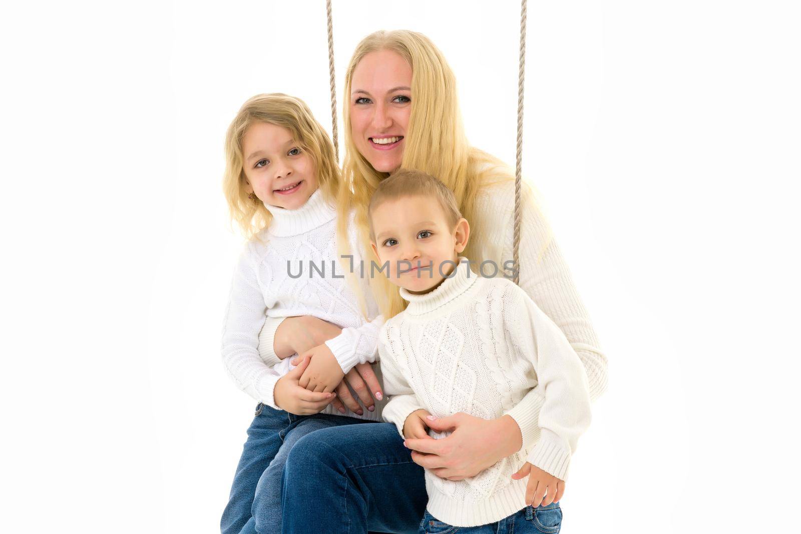 Happy Family of Mother and Two Kids Sitting Together on Rope Swing, Smiling Mom Hugging Her Son and Daughter Wearing White Sweaters and Jeans, Family Portrait Isolated on White Background