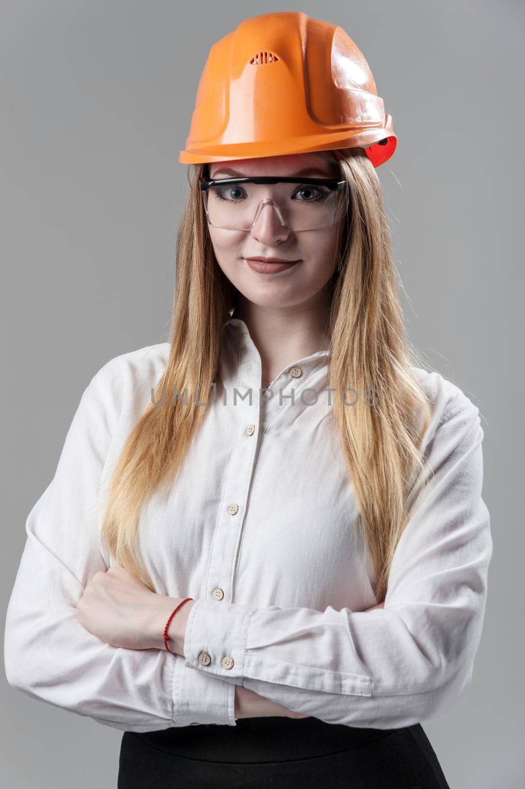 Portrait of a young attractive woman with blond hair in orange helmet and glasses on a neutral gray background.