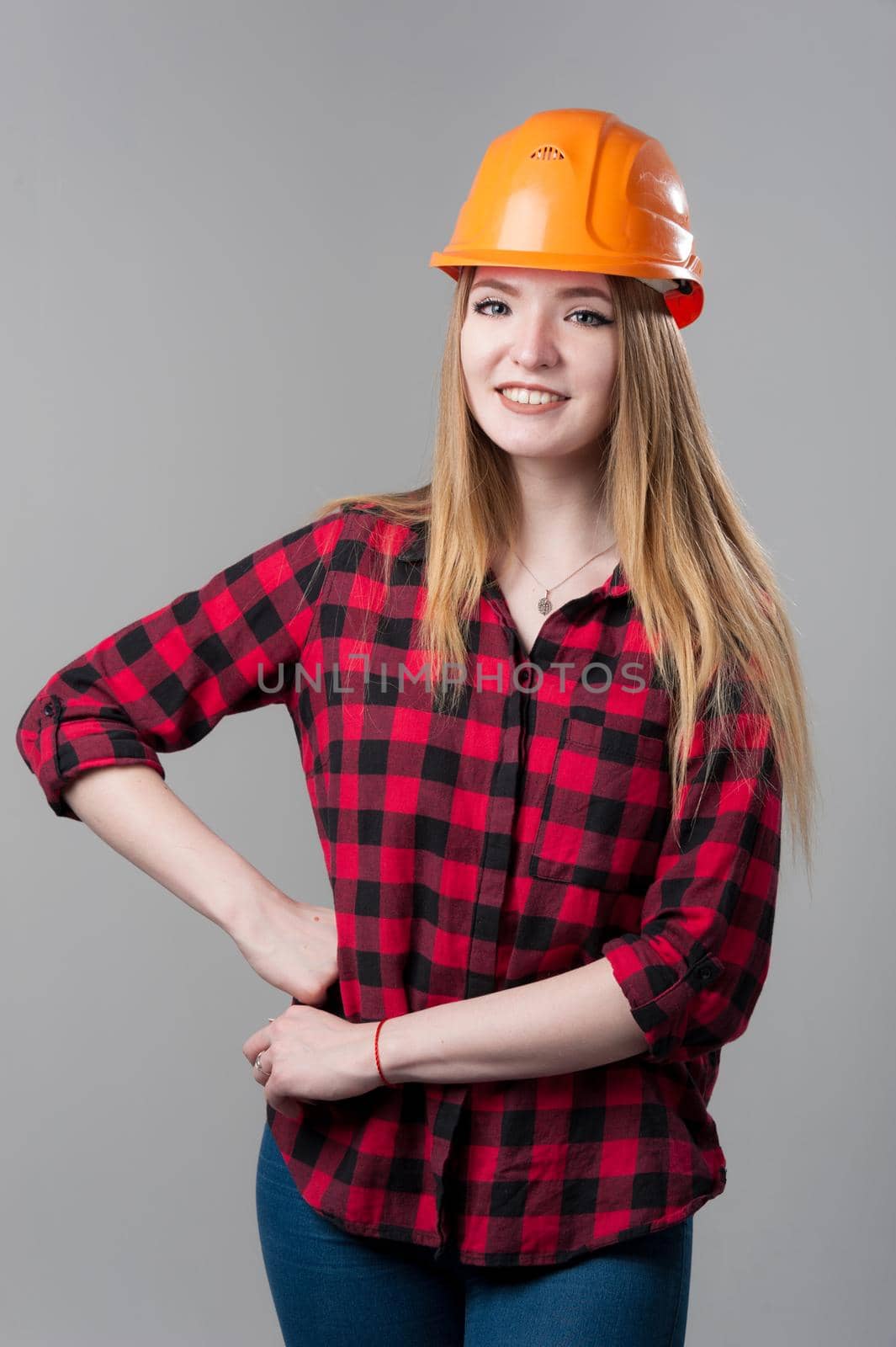 Portrait of a young attractive woman with blond hair in orange helmet on a neutral gray background. by bashta