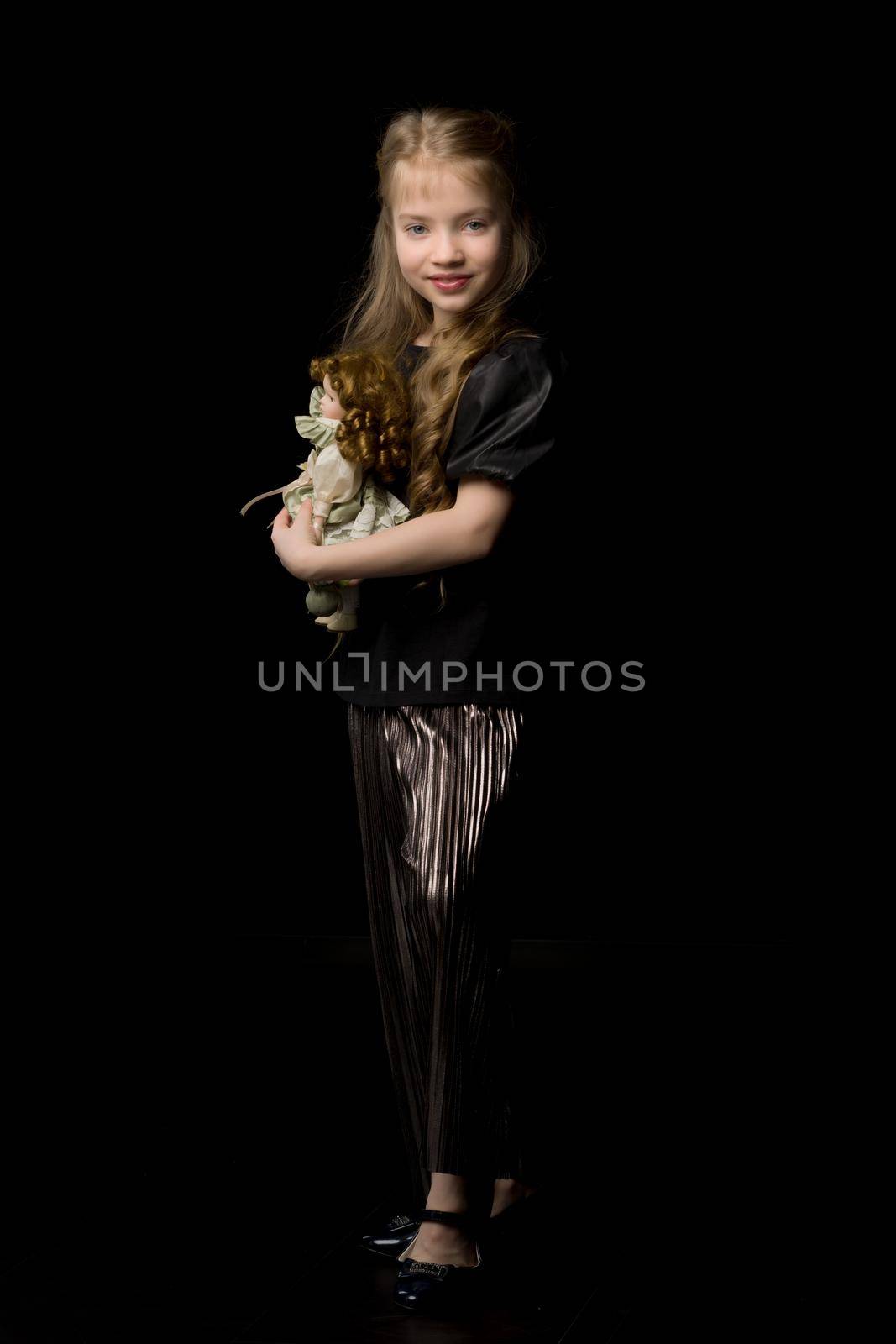 Cute little girl playing with a doll on a black background.