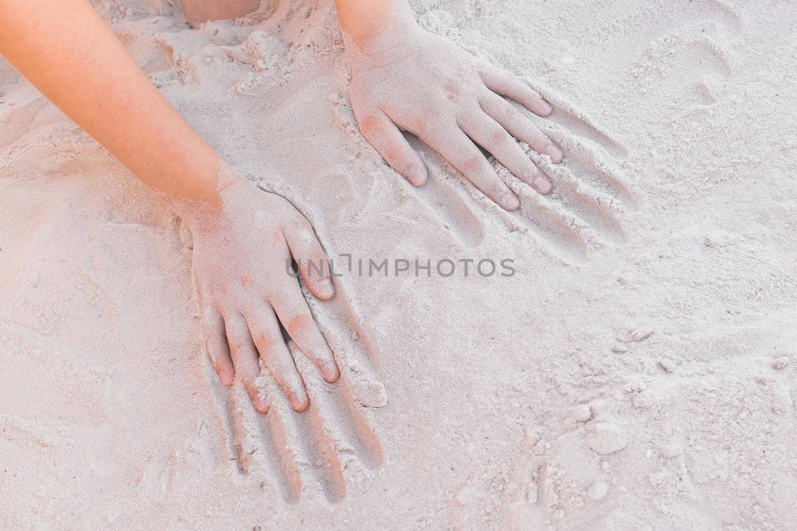 The hands of a young girl lie on a warm white beach sand background by AYDO8