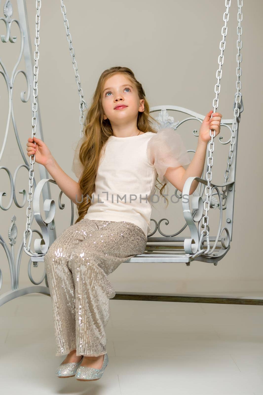 Beautiful little girl swinging in the studio on a swing. Concept of a happy childhood, family well-being.