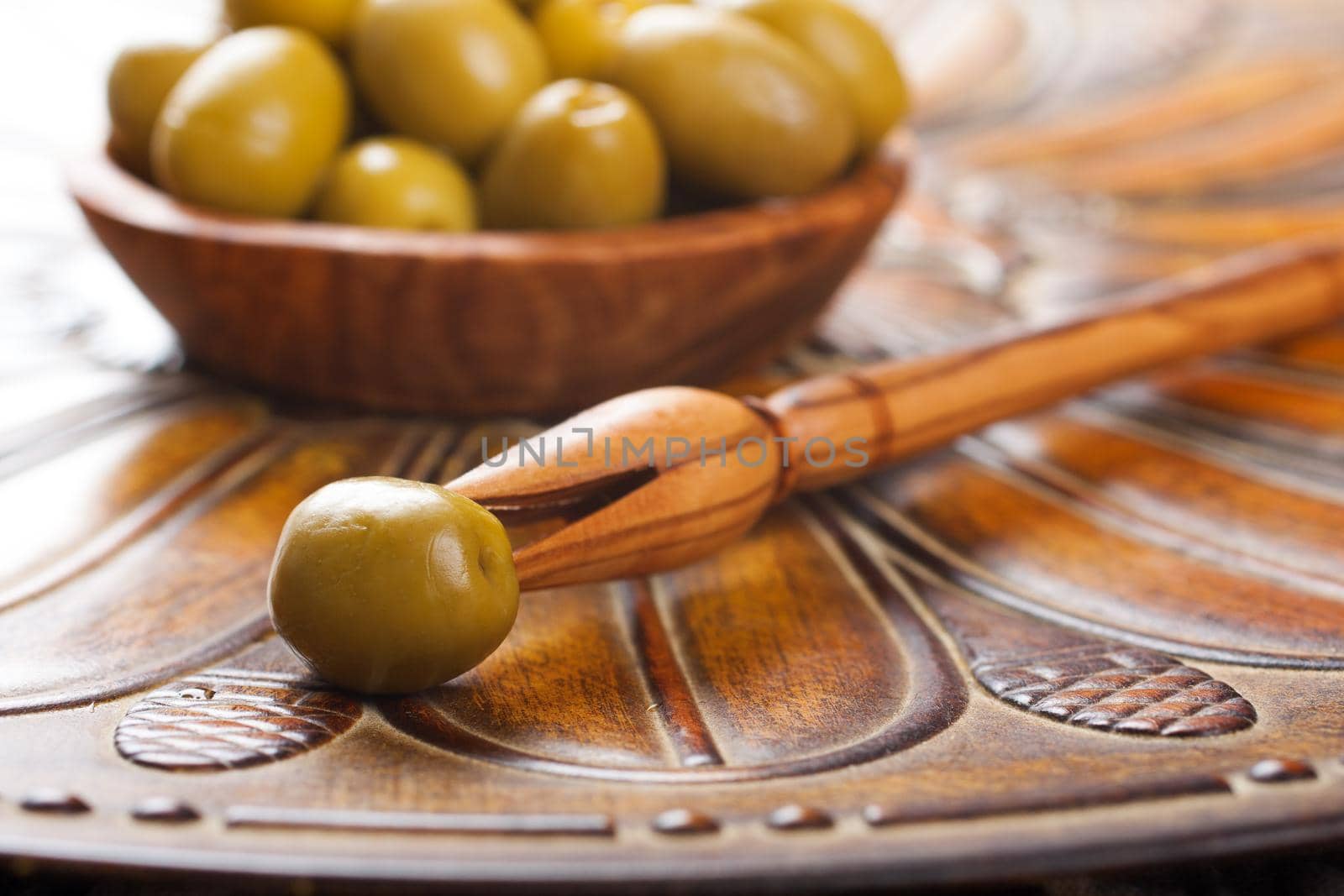 Stick with olive and bowl filled with green olives on a rustic wooden background. Selective focus.