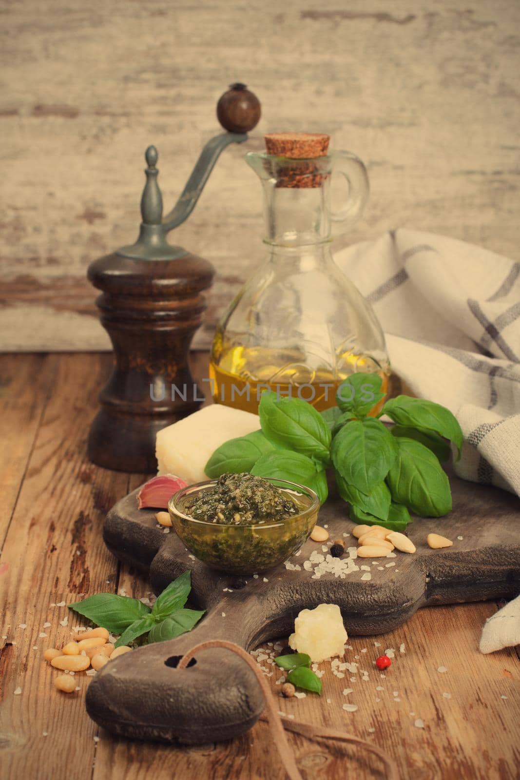 Homemade green pesto in glass bawl on a rustic wooden cutting board and fresh ingredients. Selective focus. Retro style toned.