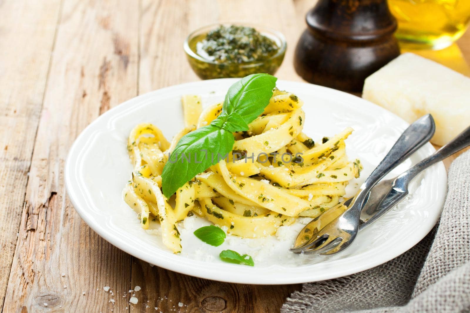 Cooked homemade tagliatelle pasta with green pesto sauce, grated pecorino cheese and basil on white plate on old wooden background.