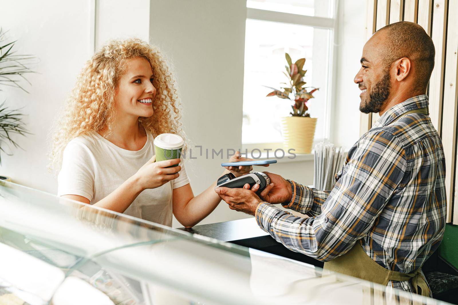 Woman customer of coffee shop paying for coffee through mobile phone using contactless technology close up