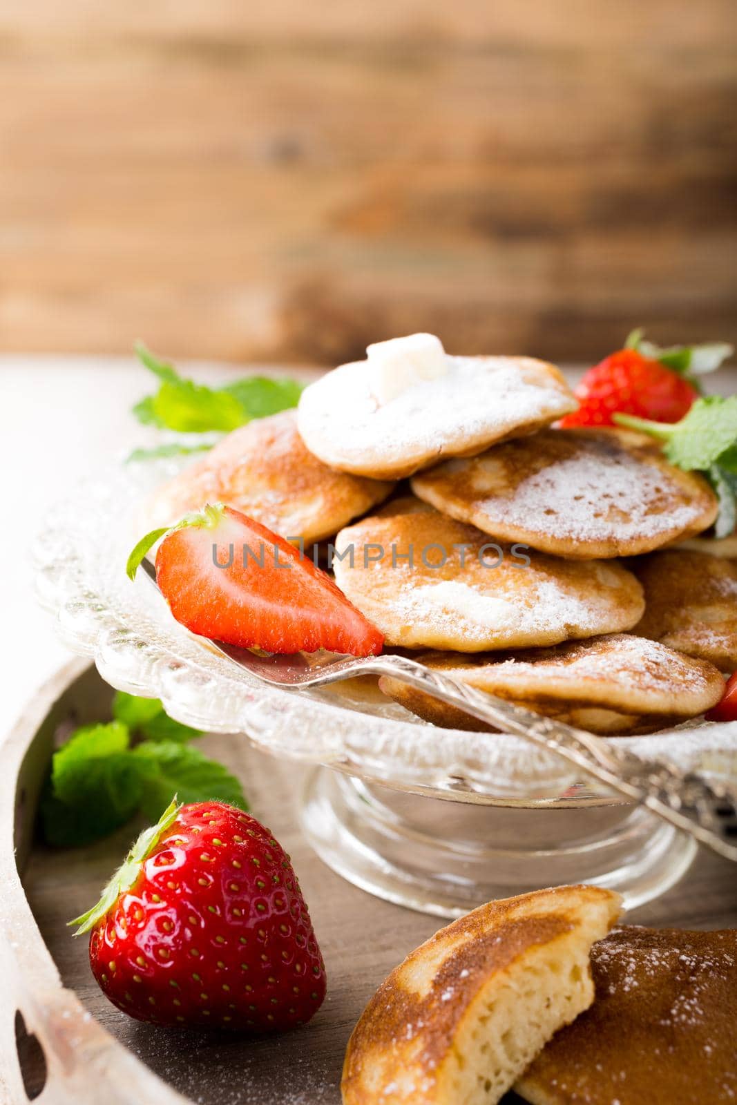 Dutch mini pancakes called poffertjes with strawberries and mint, sprinkled with powdered sugar. Healthy food concept with copy space.