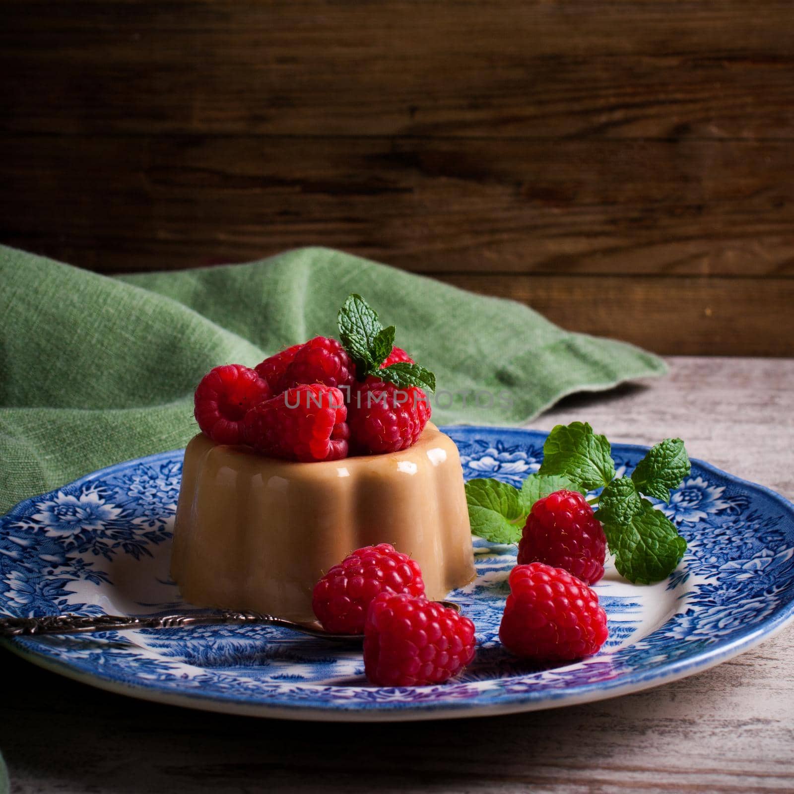 Italian dessert coffee panna cotta served on a blue plate with raspberries and fresh mint on vintage wooden bckground. Selective focus. Retro style toned.