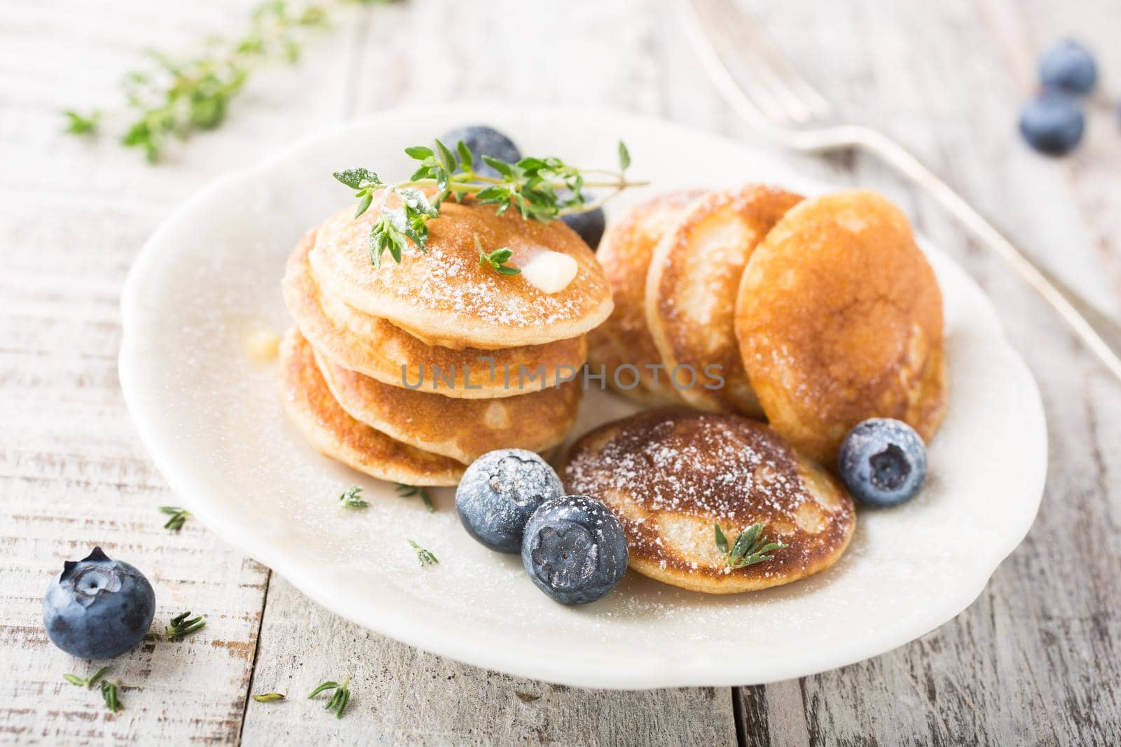 Dutch mini pancakes called poffertjes with blueberries and thyme, sprinkled with powdered sugar. Healthy food concept.