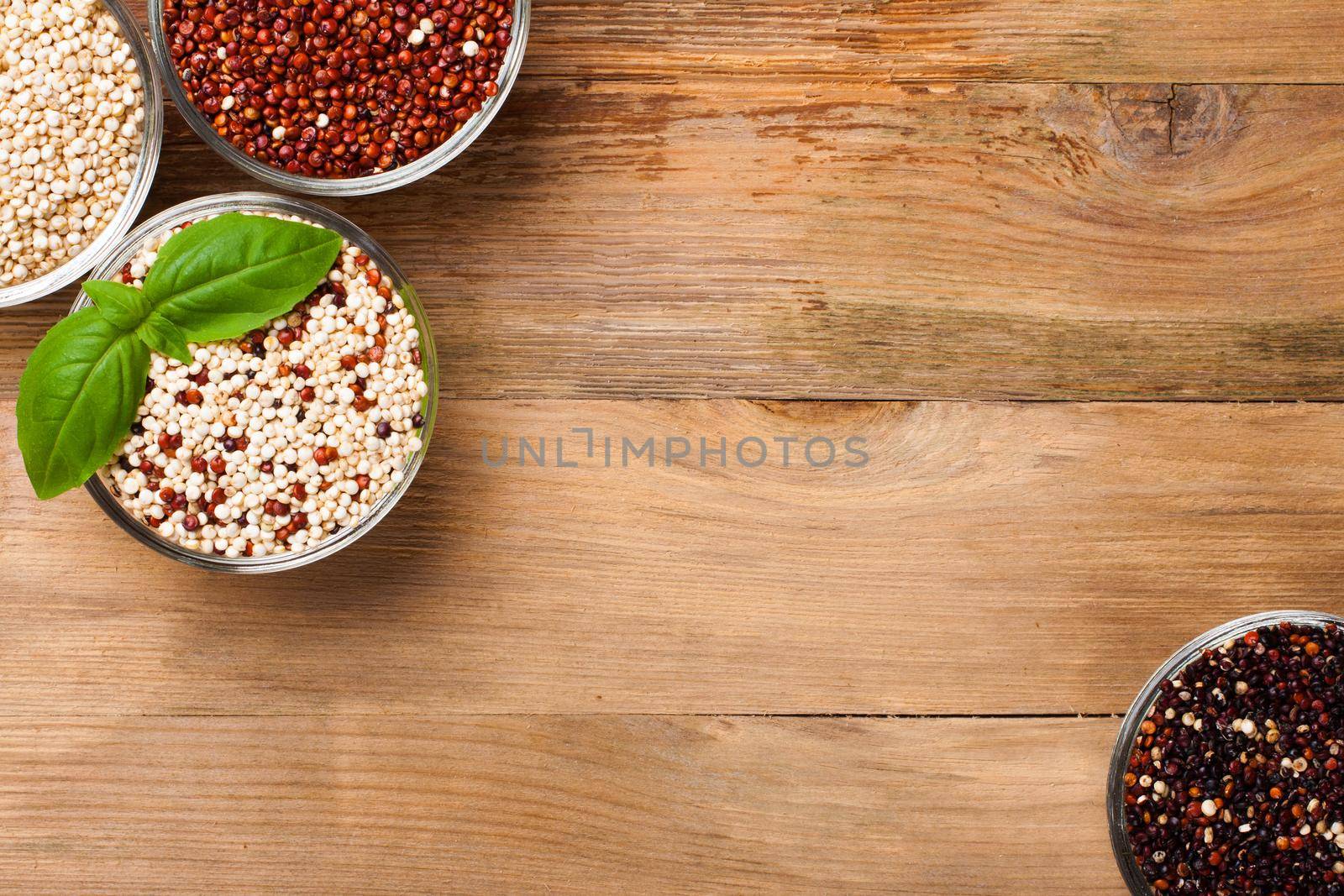 White, red, black and mixed raw quinoa, South American grain, in glass bowls with basil leaves on old rustic wooden background. Top view. Background with copy space.