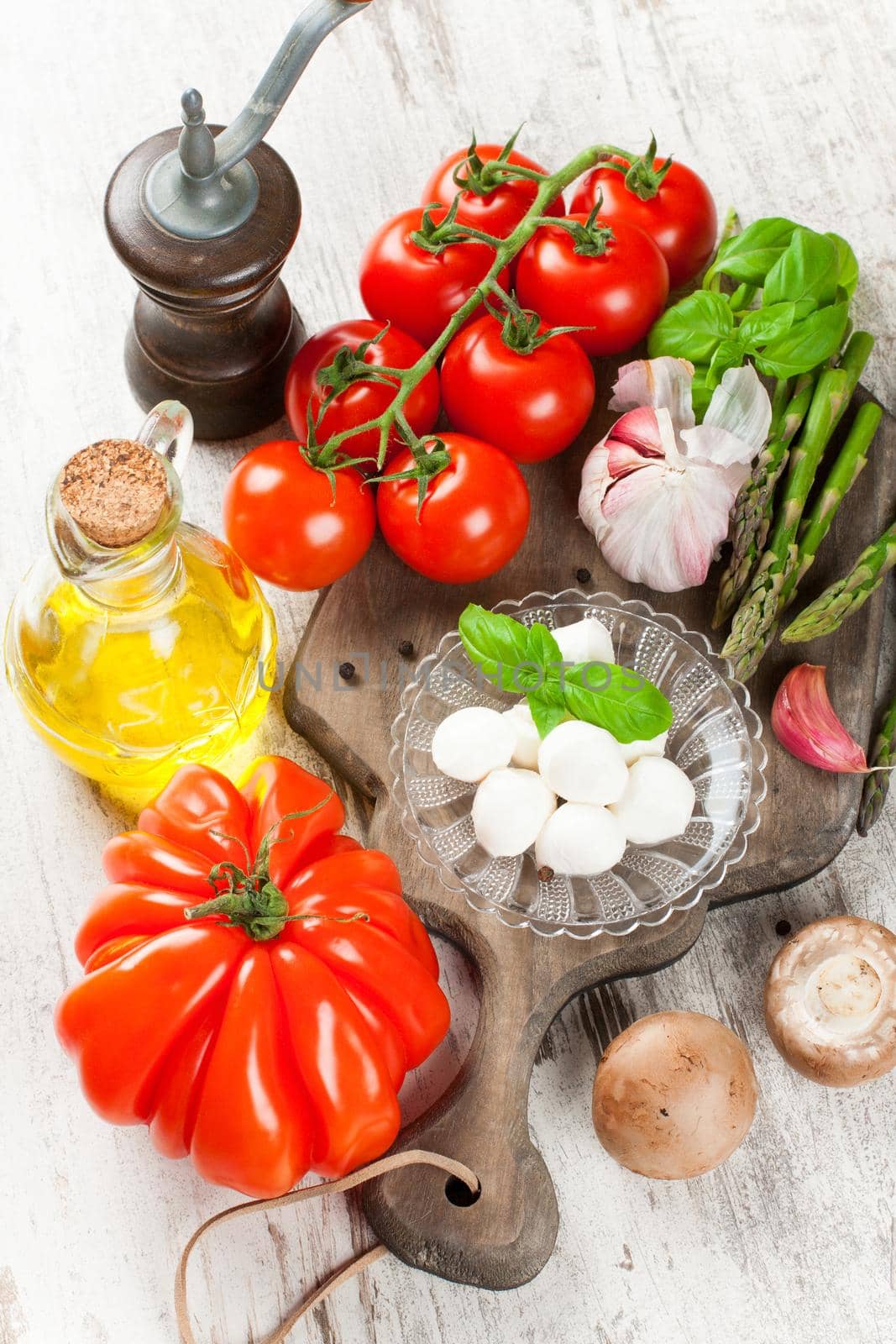 Italian food background, with tomatoes, basil, mushrooms, mozzarella balls, olive oil on vintage wooden cutting board. Healthy food concept.