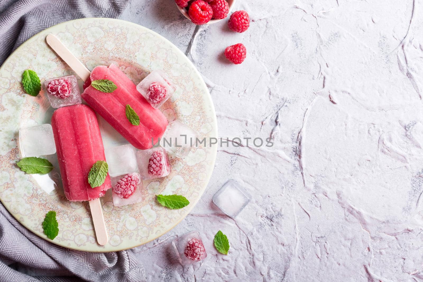 Homemade raspberry popsicles on plate with ice and berries. Summer food concept with copy space for text. Top view.