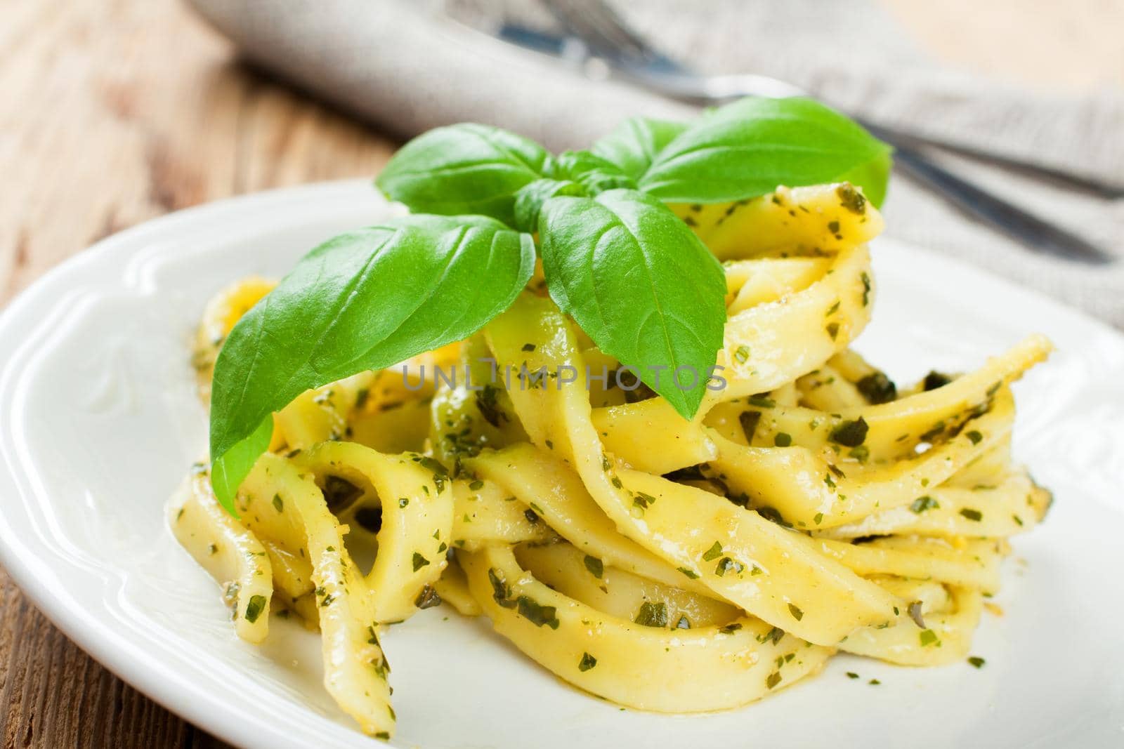 Pasta tagliatelle with green pesto sauce and basil on white plate on old wooden background. Selective focus.