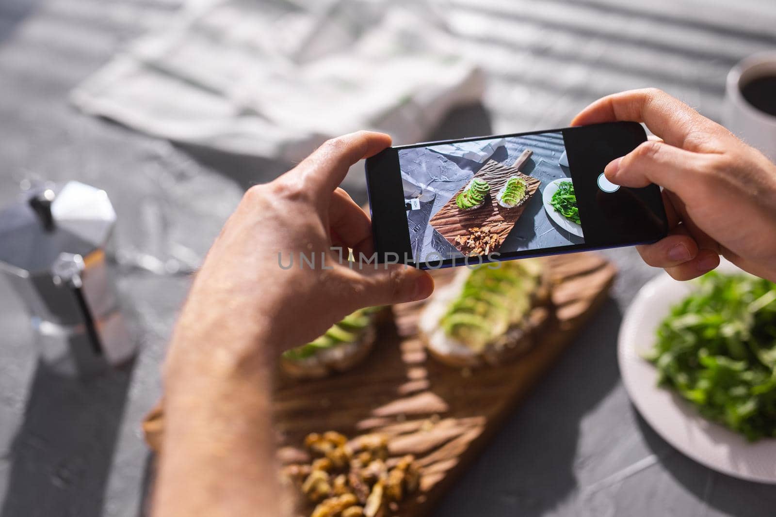 Hands take pictures on smartphone of two beautiful healthy sour cream and avocado sandwiches lying on board on the table. Social media and food