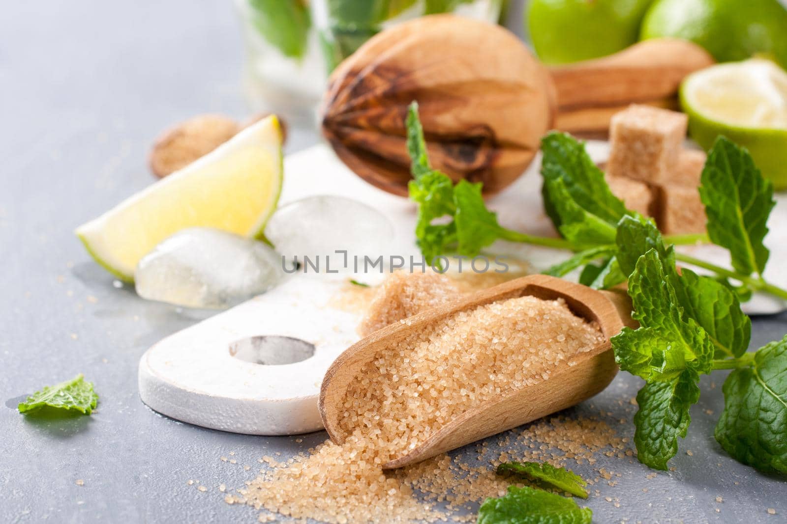 Ingredients for making mojitos. Ice, fresh mint leaves sugar cubs, lime and glass on white cutting board