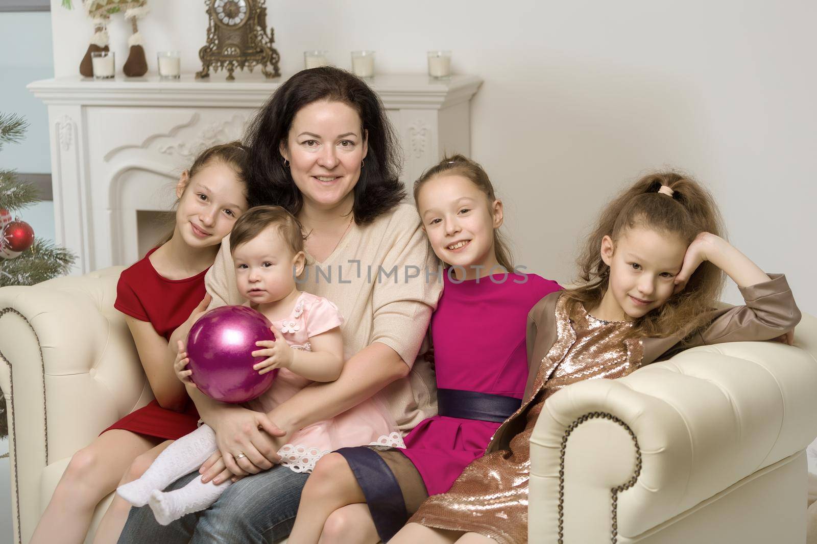Studio Portrait of Happy Family of Mother and Three Daughters, Smiling Mom and Cute Three Sisters Sitting on the Sofa and Looking at the Camera, Happy Parenting and Childhood Concept