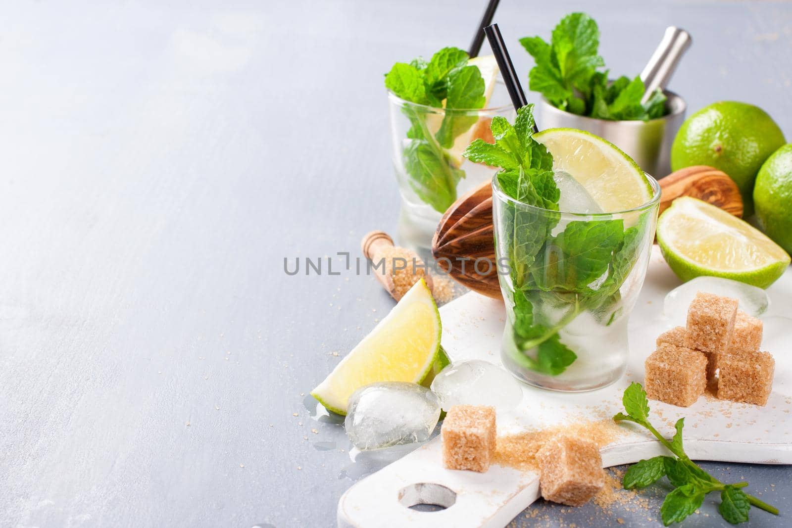 Ingredients for making mojitos. Ice, fresh mint leaves sugar cubs, lime and glass on white cutting board. Selective focus. Food background with empty copy space.