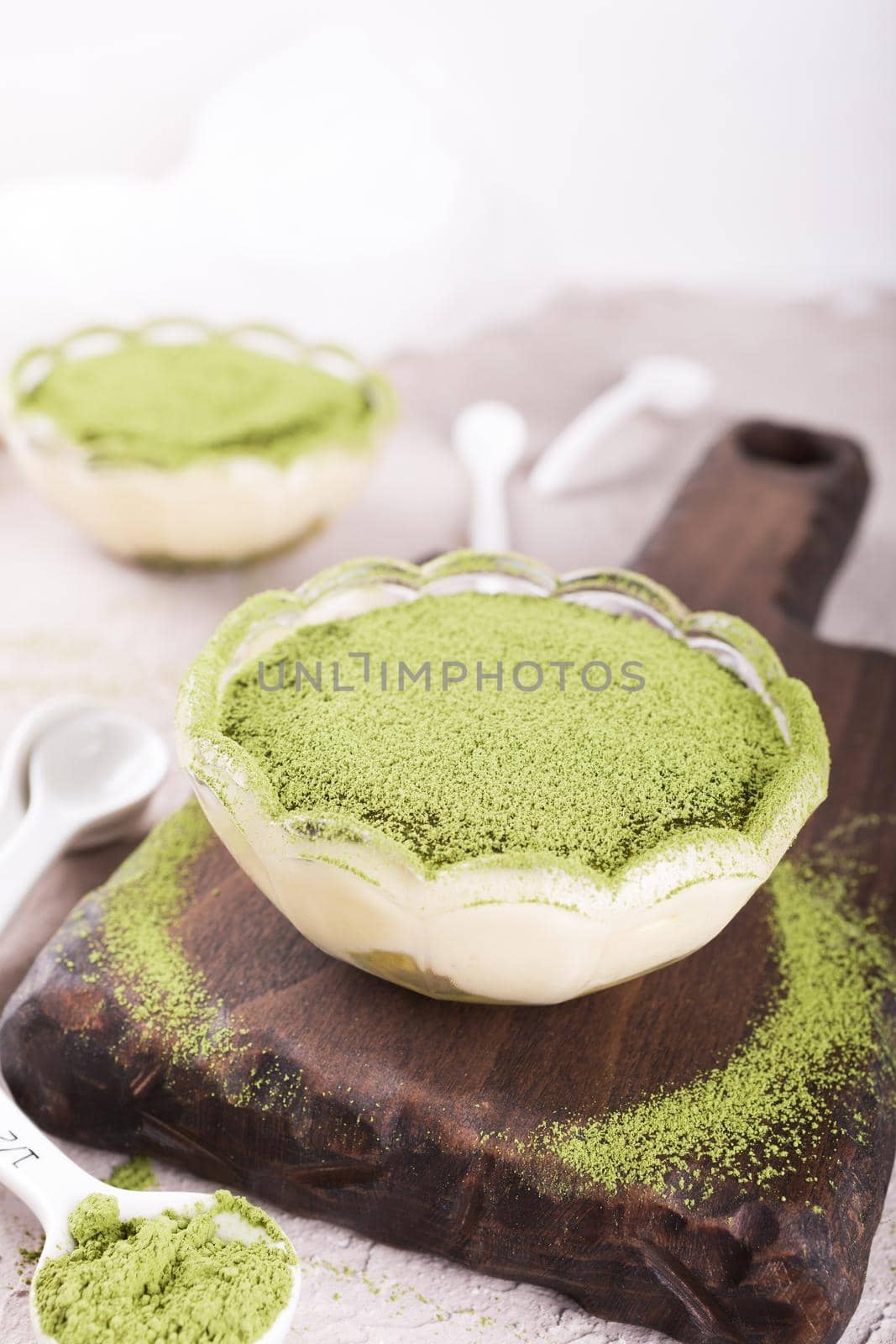 Tiramisu cake with green matcha tea in glass bowl on wooden cutting board.