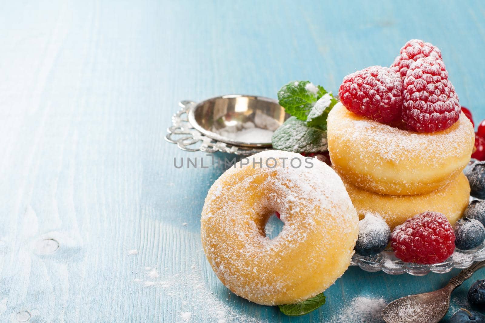 Morning breakfast with mini donuts and berries on plate under powdered sugar on blue wooden background. Tasty donuts closeup. Doughnut. Copy space.