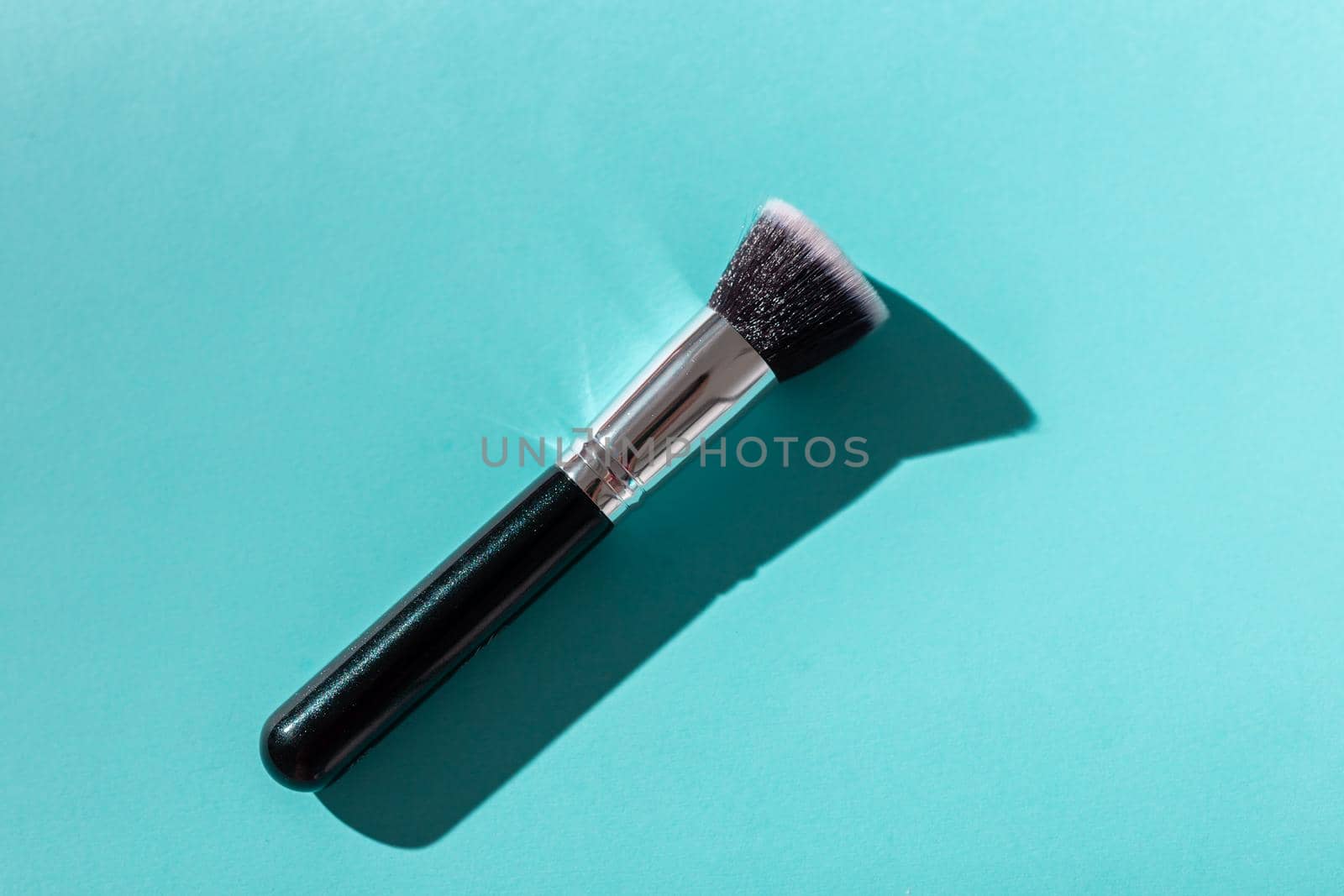 Make up brush on turquoise background, top view