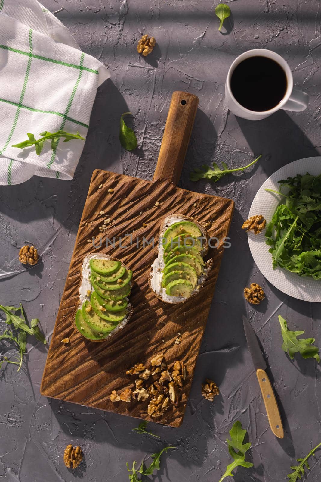 Top view of sour cream bread and avocado sandwiches with nuts and fresh herbs and cup of coffee on gray textured background. Healthy breakfast. by Satura86