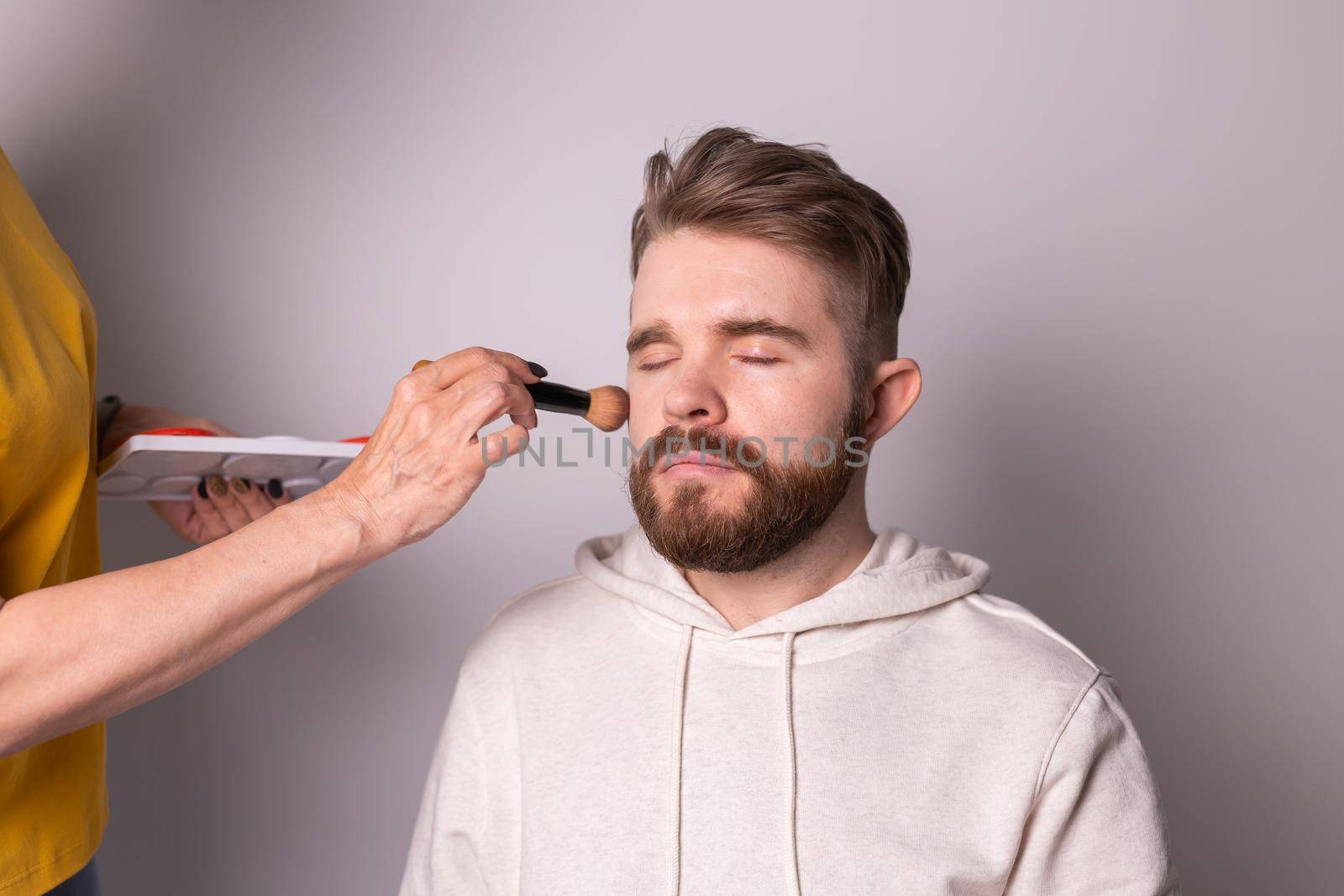 Professional makeup artist doing young man makeup in studio