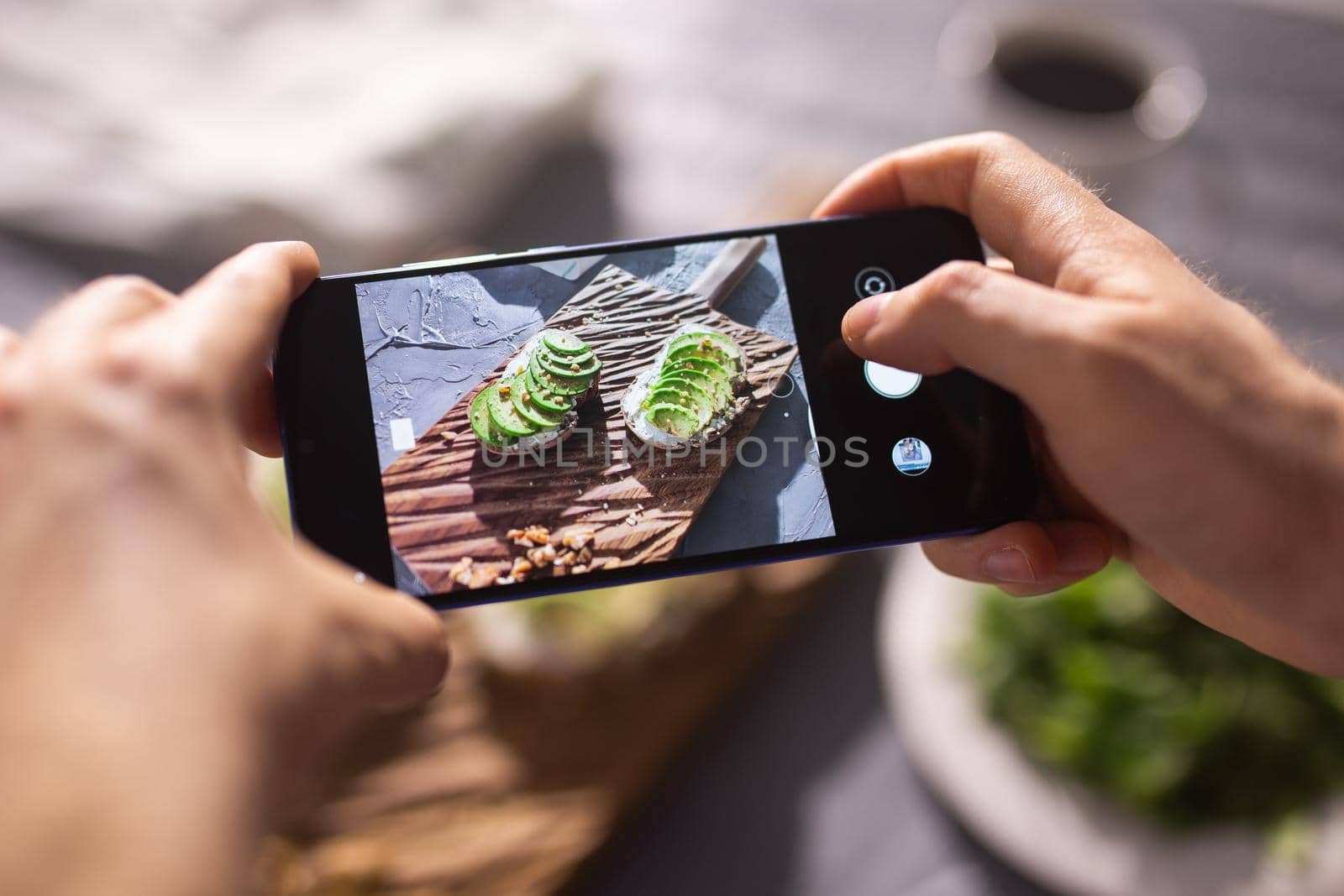 Hands take pictures on smartphone of two beautiful healthy sour cream and avocado sandwiches lying on board on the table. Social media and food