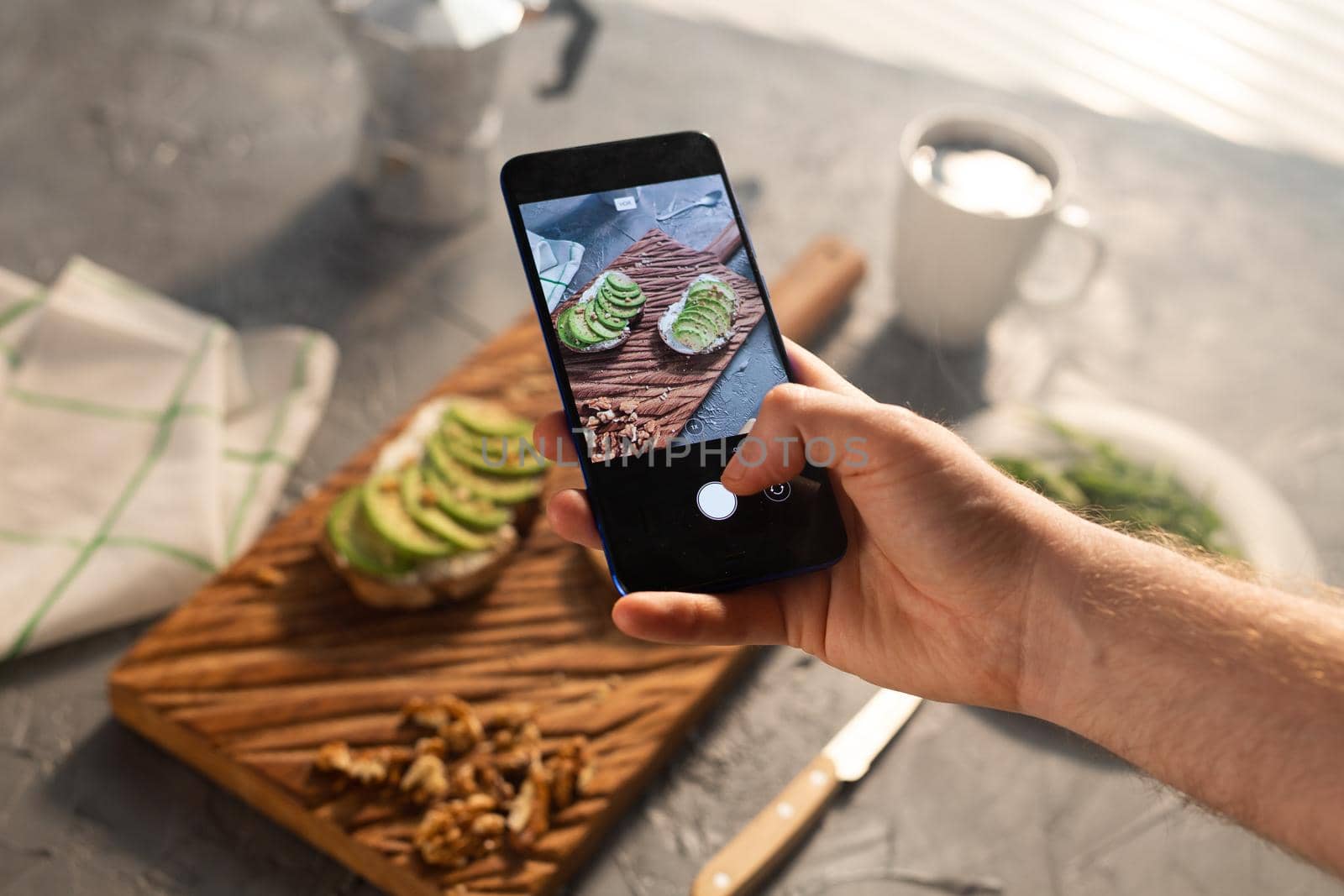 Hands take pictures on smartphone of two beautiful healthy sour cream and avocado sandwiches lying on board on the table. Social media and food