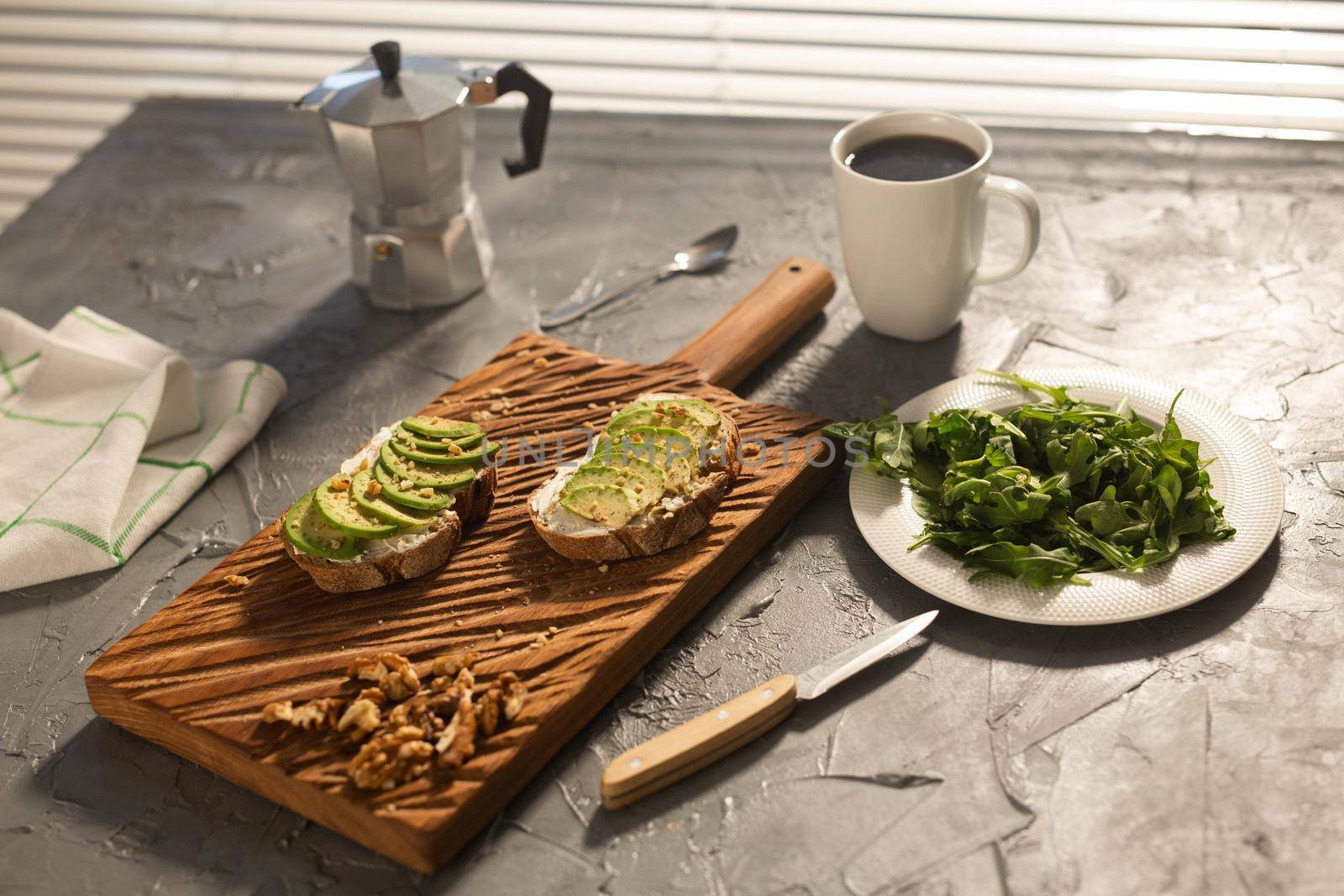 Sliced avocado on toast bread with nuts and coffee. Spinach on a plate and moka pot. Breakfast and healthy food