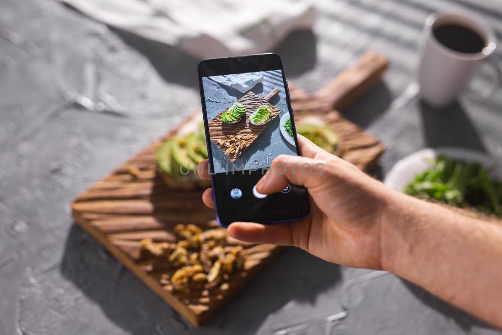 Hands take pictures on smartphone of two beautiful healthy sour cream and avocado sandwiches lying on board on the table. Social media and food