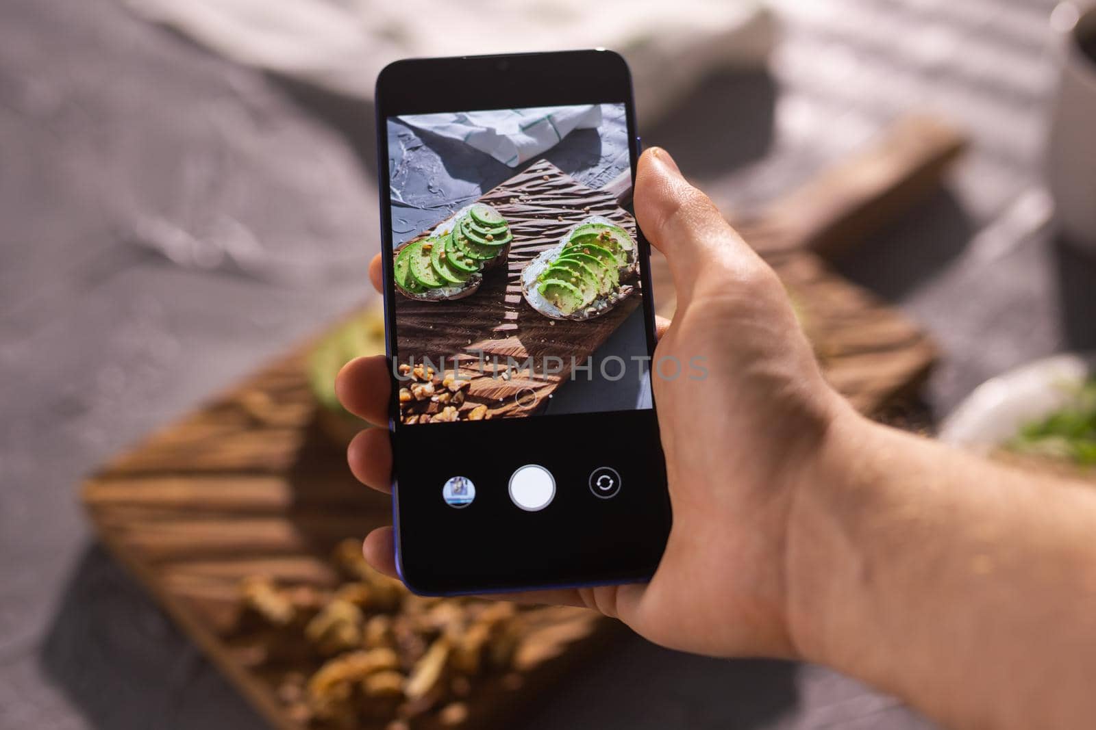 Hands take pictures on smartphone of two beautiful healthy sour cream and avocado sandwiches lying on board on the table. Social media and food concept by Satura86