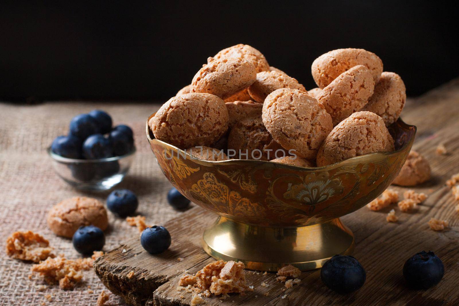 Italian almond cookie amaretti with blueberries on rustic wooden board, selective focus, law key.