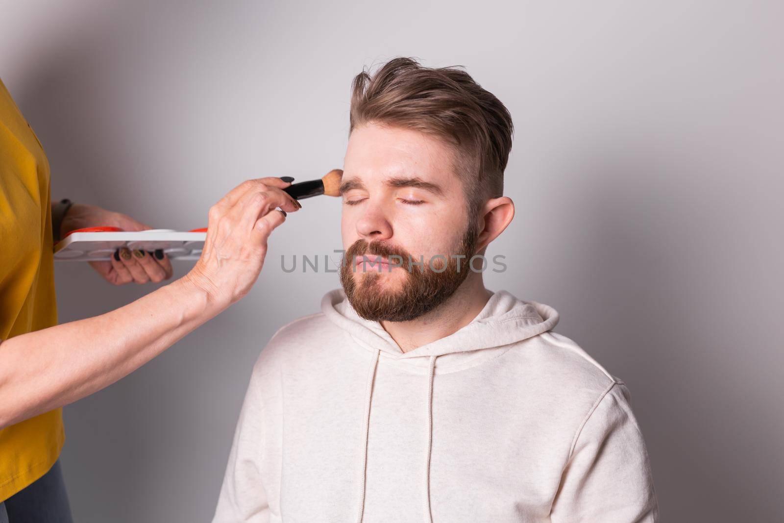 Professional makeup artist doing young man makeup in studio