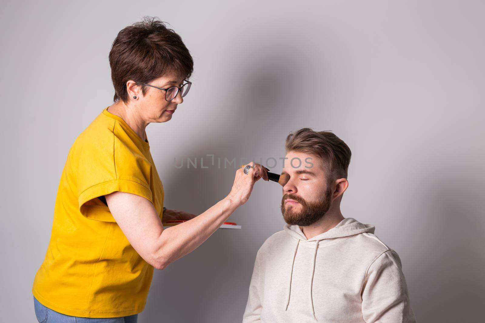 Professional makeup artist doing young man makeup in studio