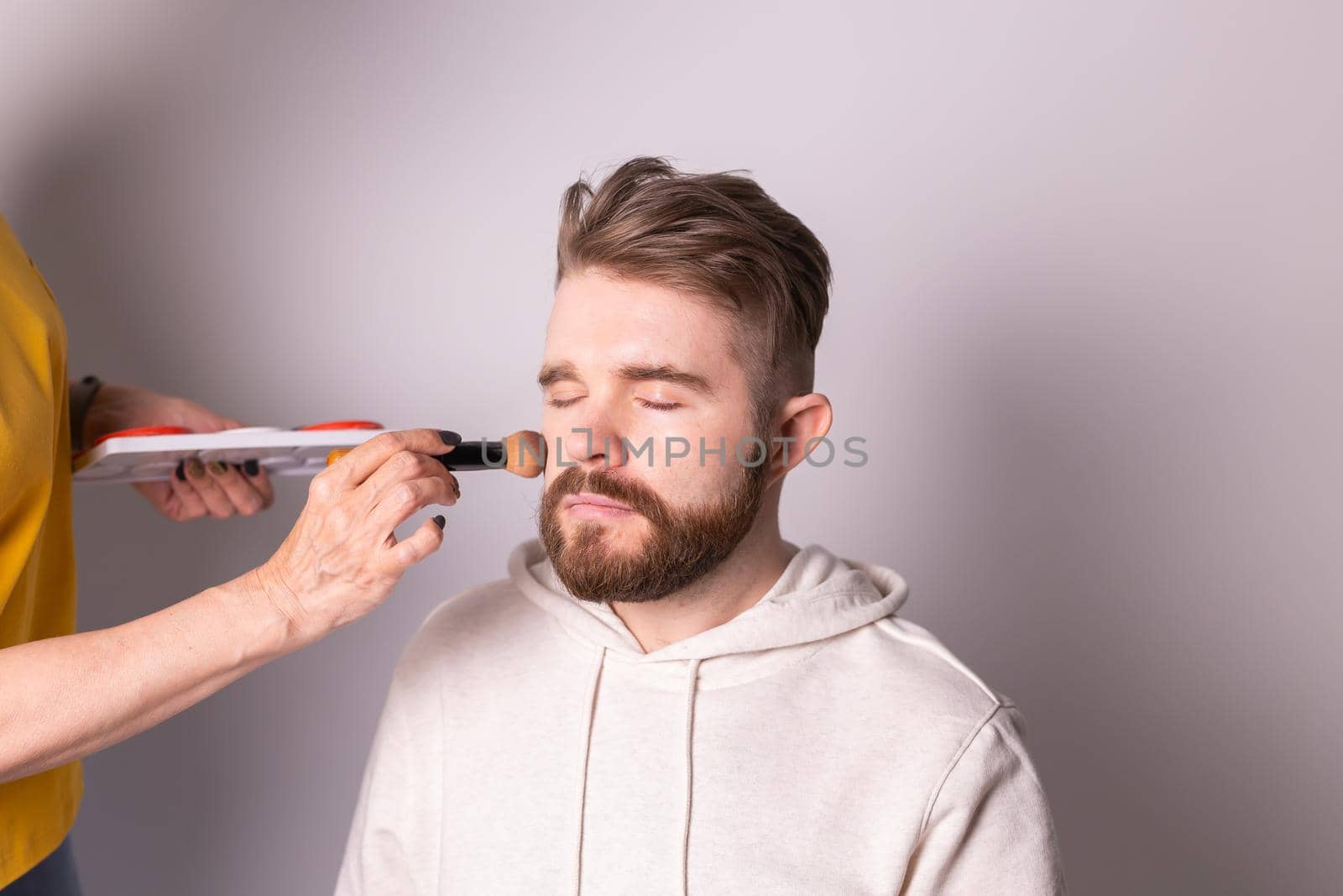 Bearded man getting makeup. Hand of visagist using brush