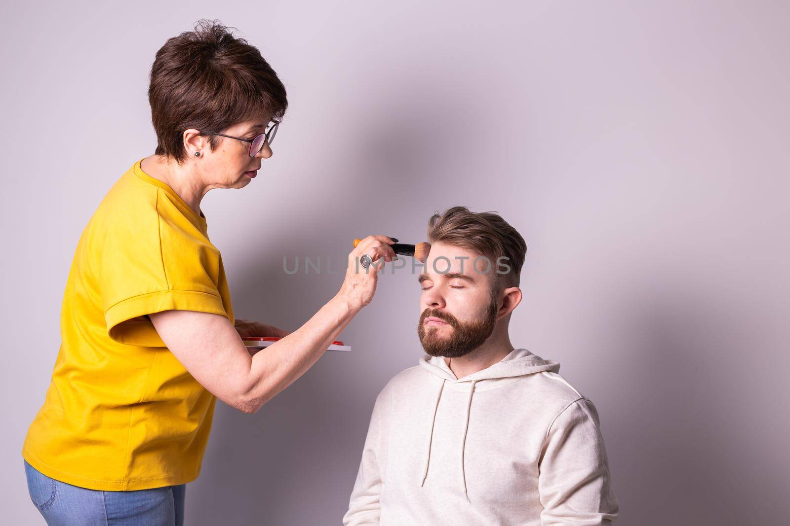 Professional makeup artist doing young man makeup in studio