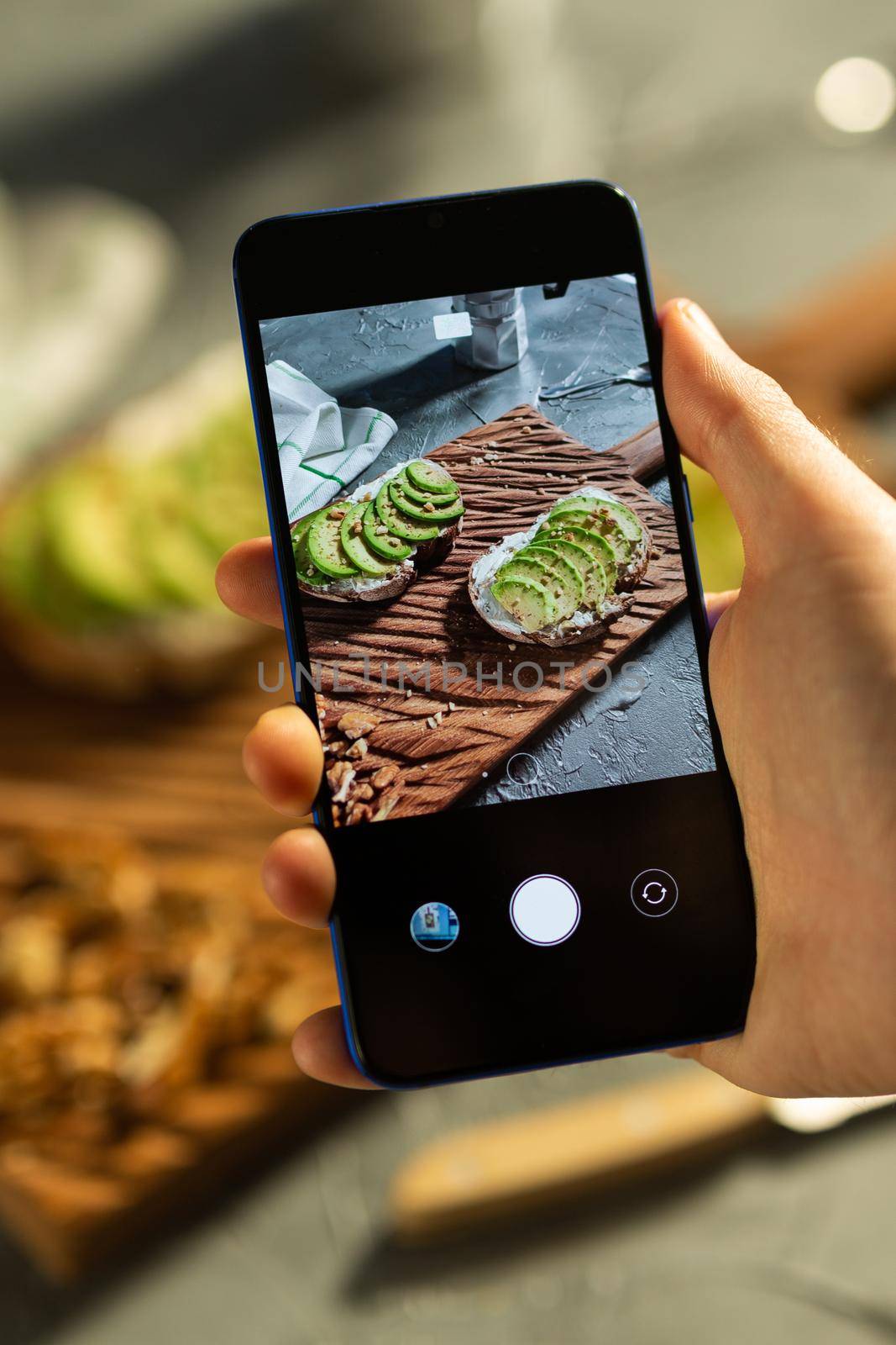 Hands take pictures on smartphone of two beautiful healthy sour cream and avocado sandwiches lying on board on the table. Social media and food concept by Satura86