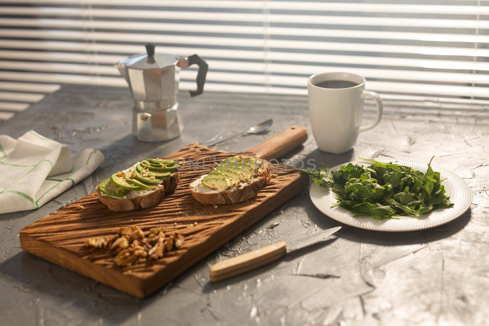 Sliced avocado on toast bread with nuts and coffee. Spinach on a plate and moka pot. Breakfast and healthy food concept. by Satura86