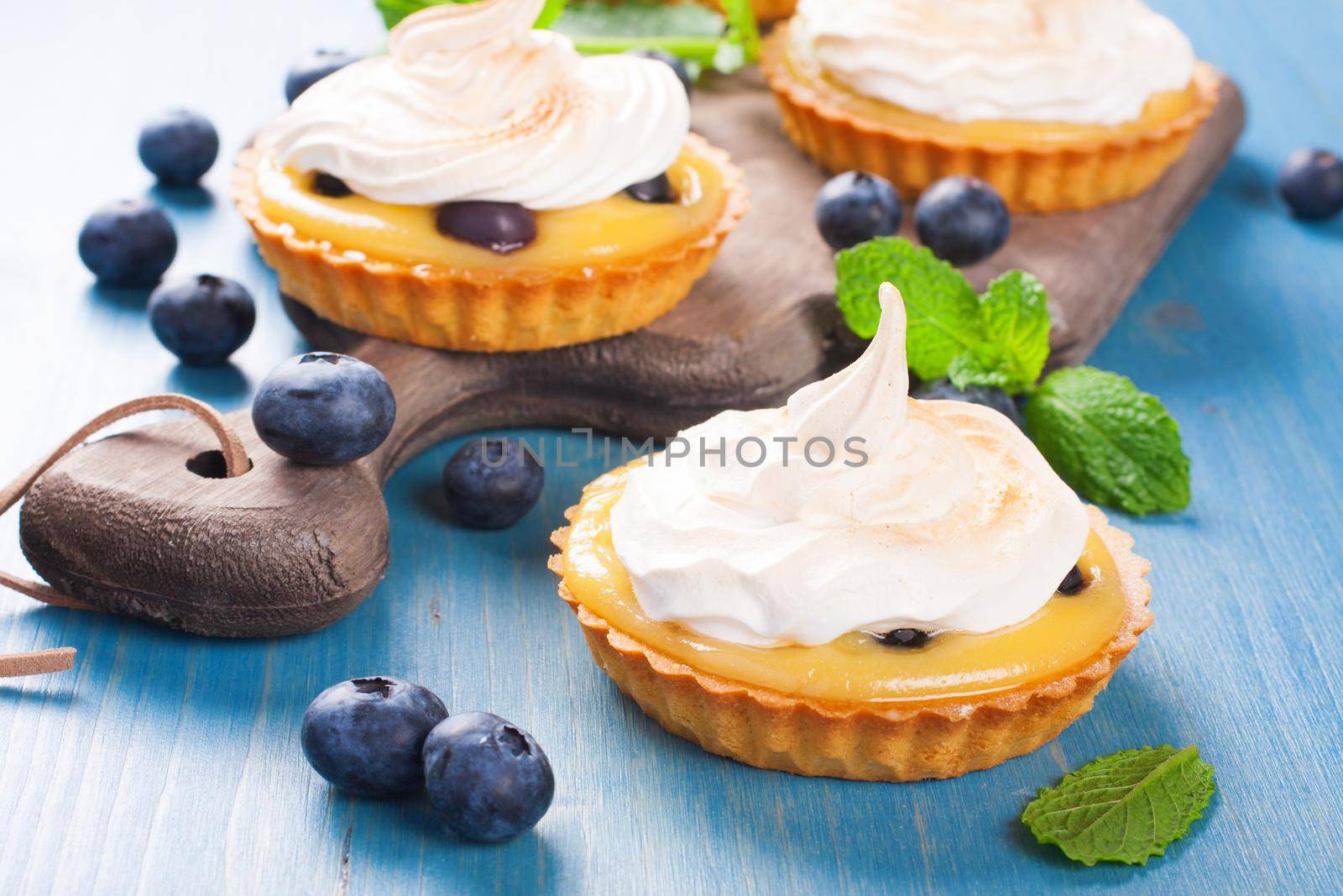 Handmade little tarts, cakes, tartlets with lime curd, meringue en berries on old rustik board on blue wooden background. Selective focus.