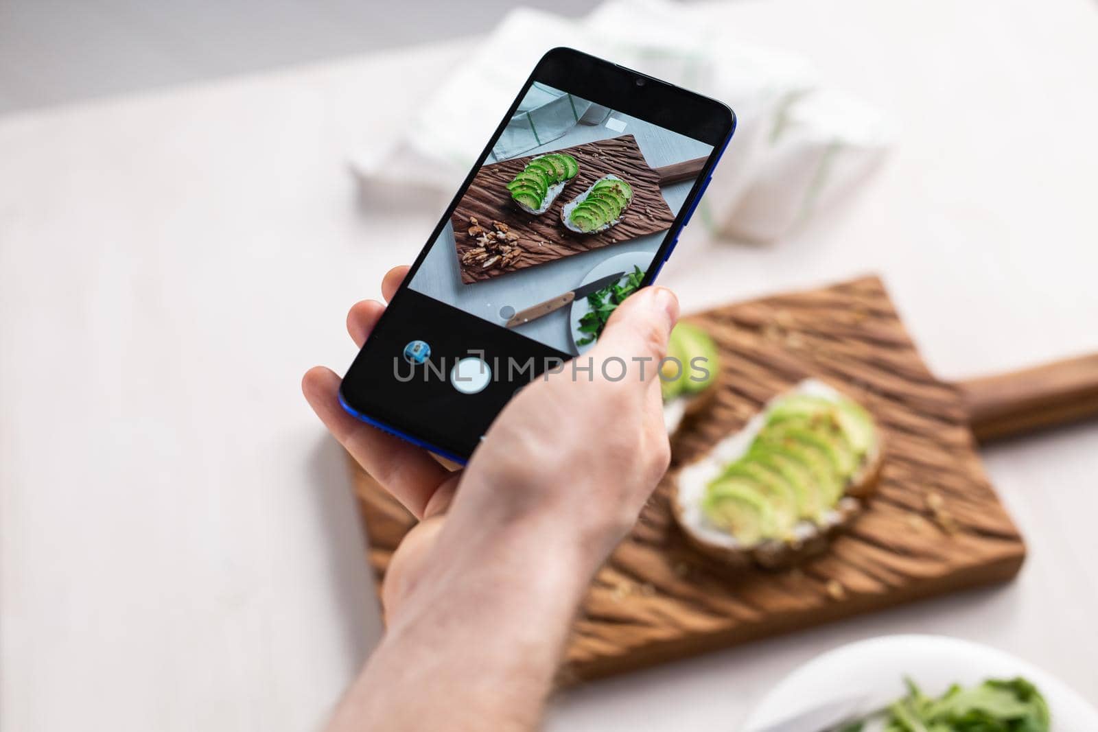 Hands take pictures on smartphone of two beautiful healthy sour cream and avocado sandwiches lying on board on the table. Social media and food concept by Satura86