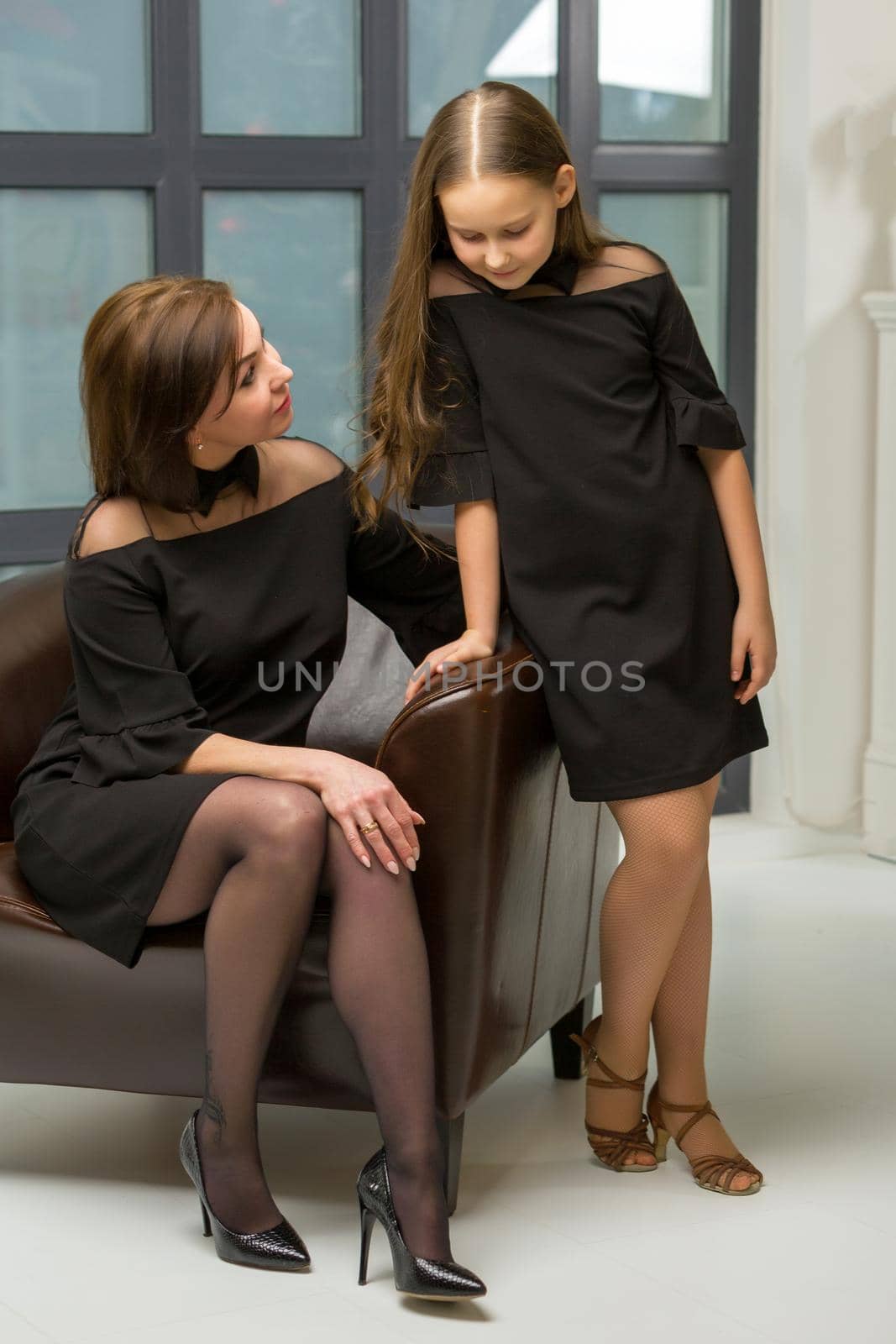 Happy family, mom and daughter near a large panoramic window, in the studio.