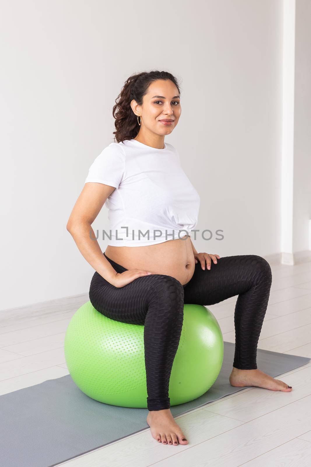 A young pregnant woman doing relaxation exercise using a fitness ball while sitting on a mat. by Satura86