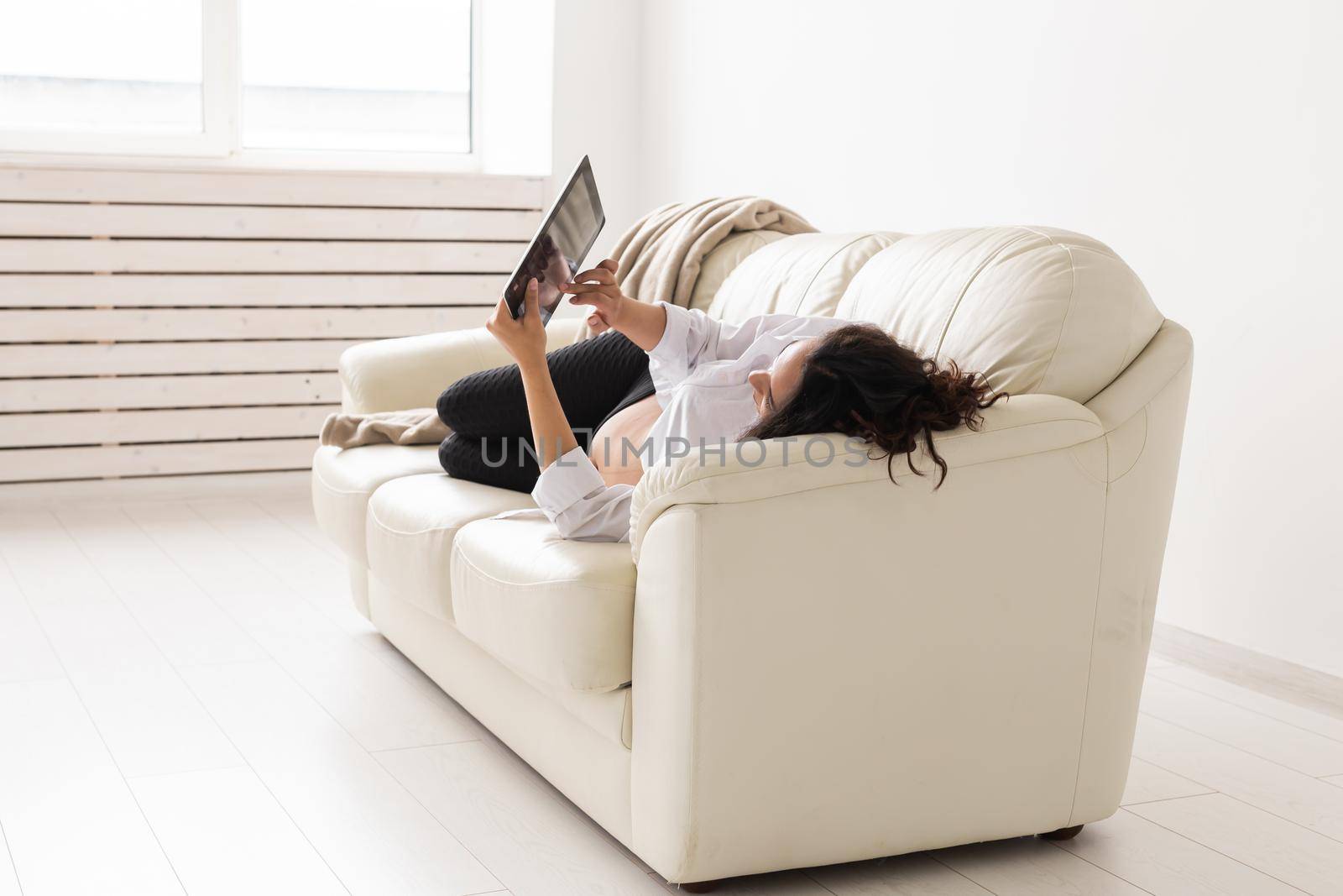 Latin pregnant woman using tablet computer sitting on sofa at home. Pregnancy and information for parenthood