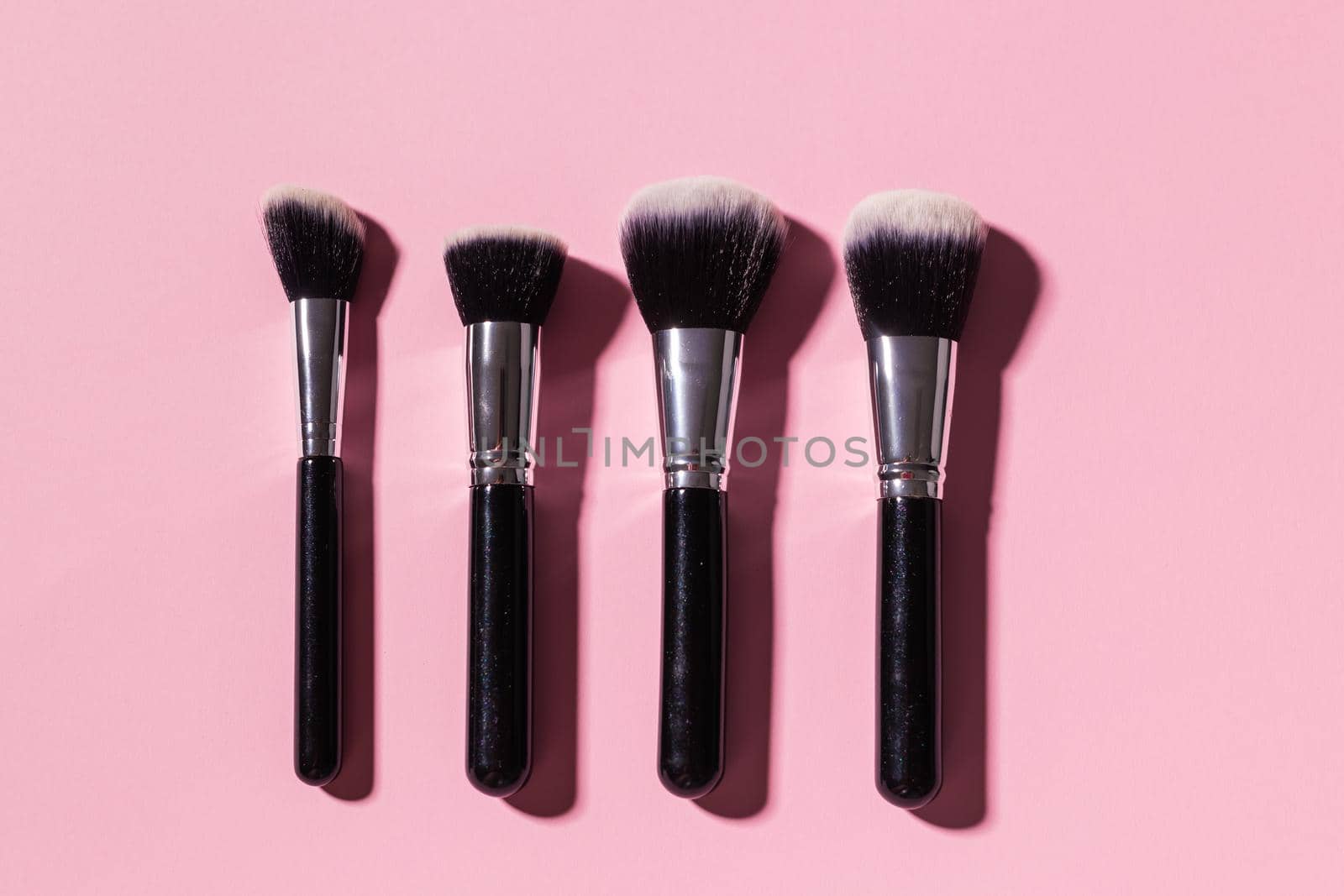 Various make-up brushes on pink background, top view. Cosmetics and beauty