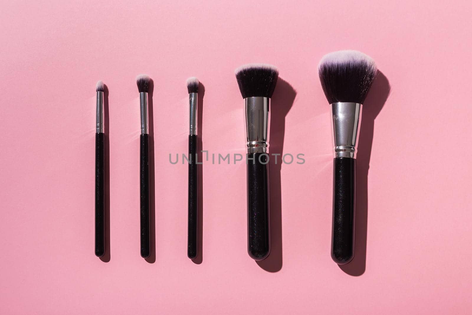 Various make-up brushes on pink background, top view. Cosmetics and beauty