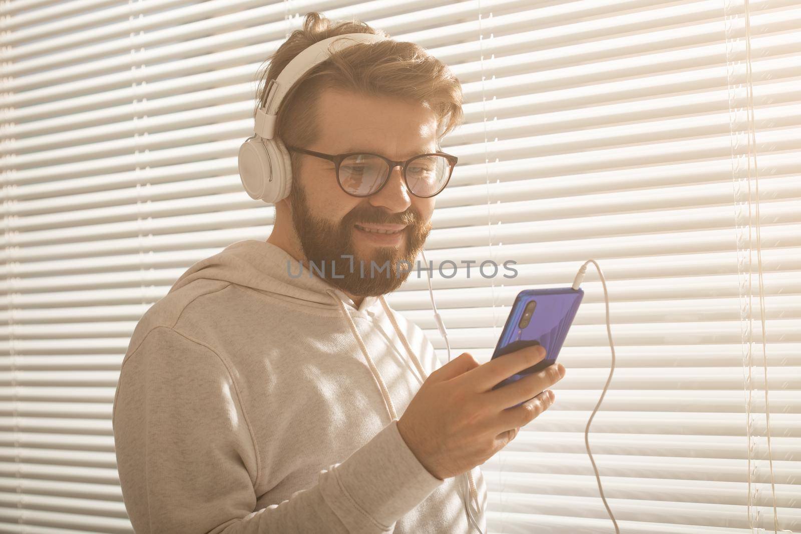 Close-up portrait of young stylish hipster man choosing favorite music in smartphone with headphones in office. Music subscription