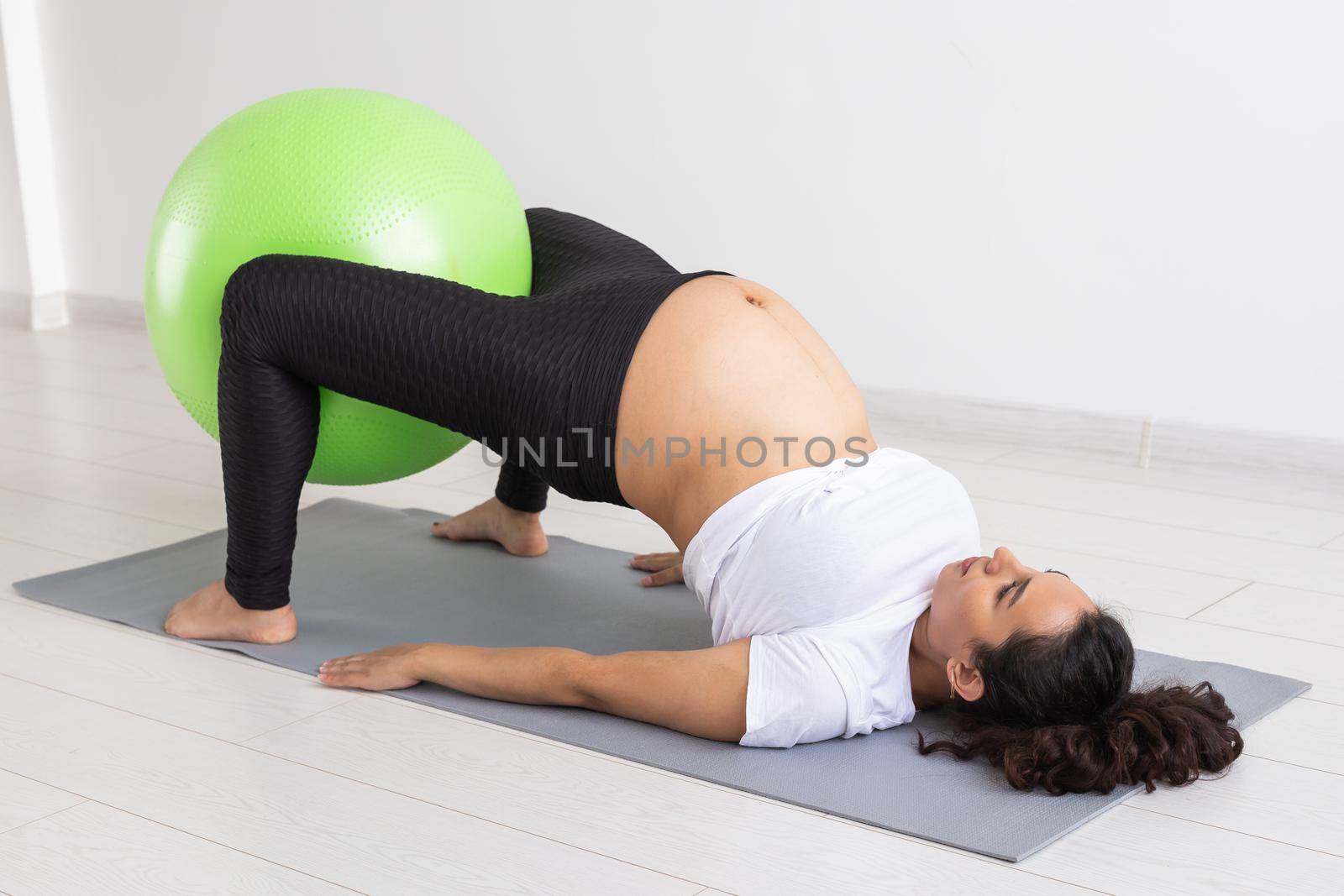 Young flexible pregnant woman doing gymnastics on rug on the floor on white background. Preparing the body for easy childbirth