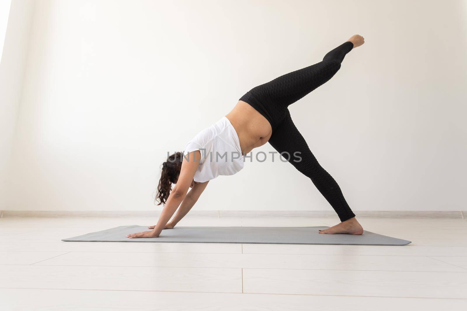 Young flexible pregnant woman doing gymnastics on rug on the floor on white background. Preparing the body for easy childbirth