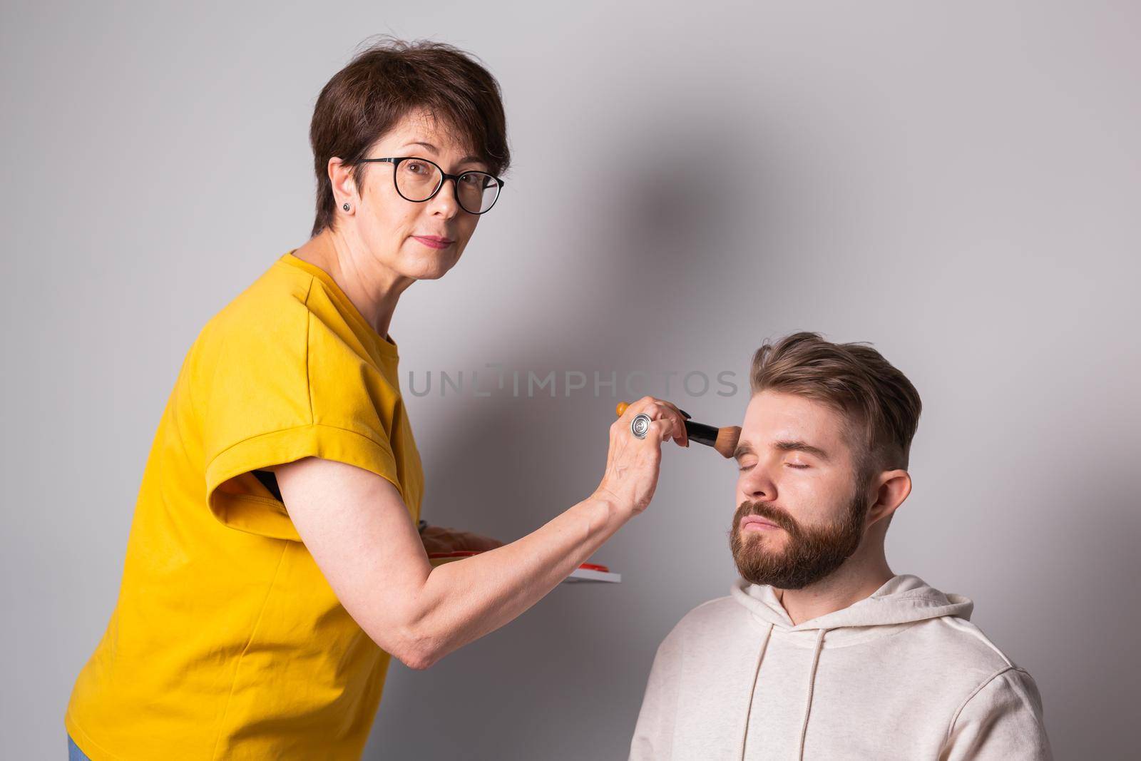 Professional makeup artist doing young man makeup in studio