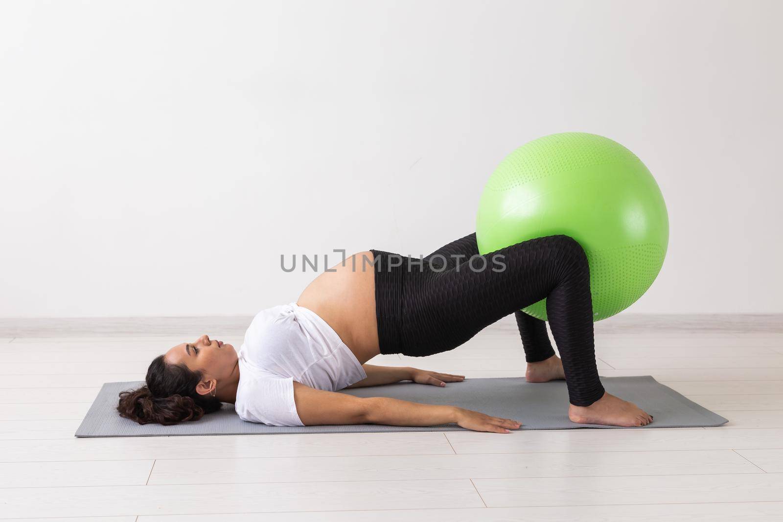 Young flexible pregnant woman doing gymnastics on rug on the floor on white background. Preparing the body for easy childbirth